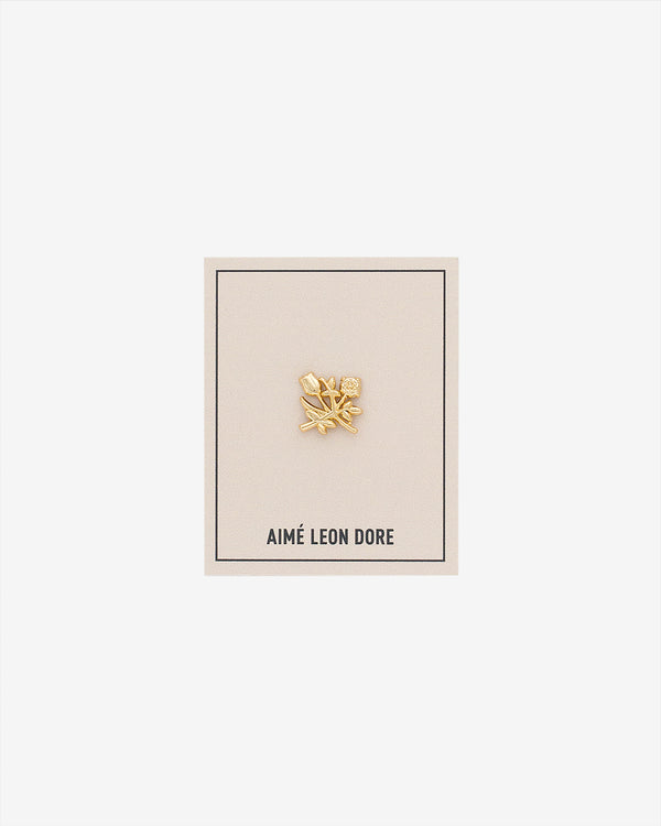 An ALD Pin shaped like a gold leaf is displayed on a beige AIMÉ LEON DORE card against a white background.