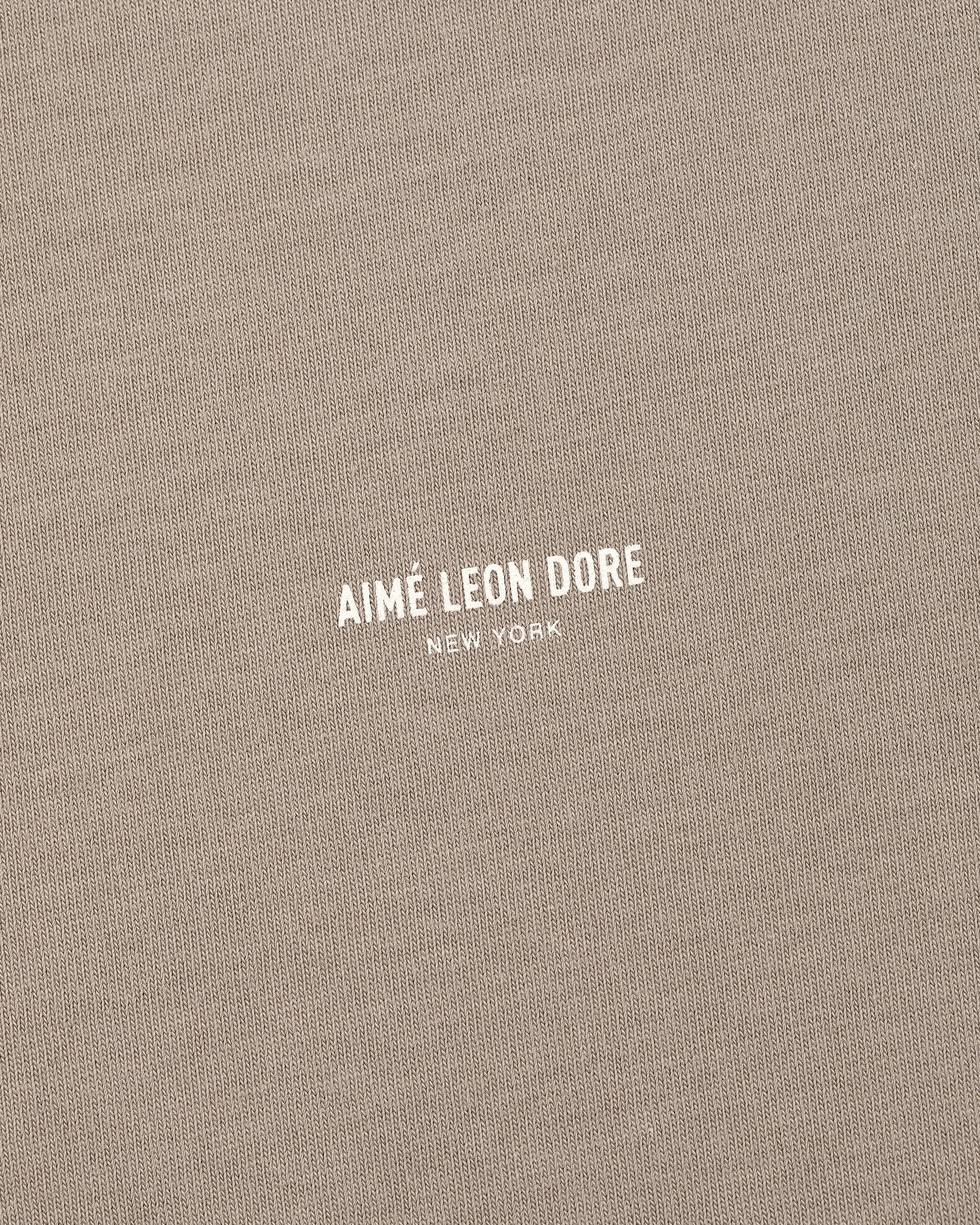 Close-up of beige Micro Logo Tee with AIMÉ LEON DORE NEW YORK printed in small white letters at the center.