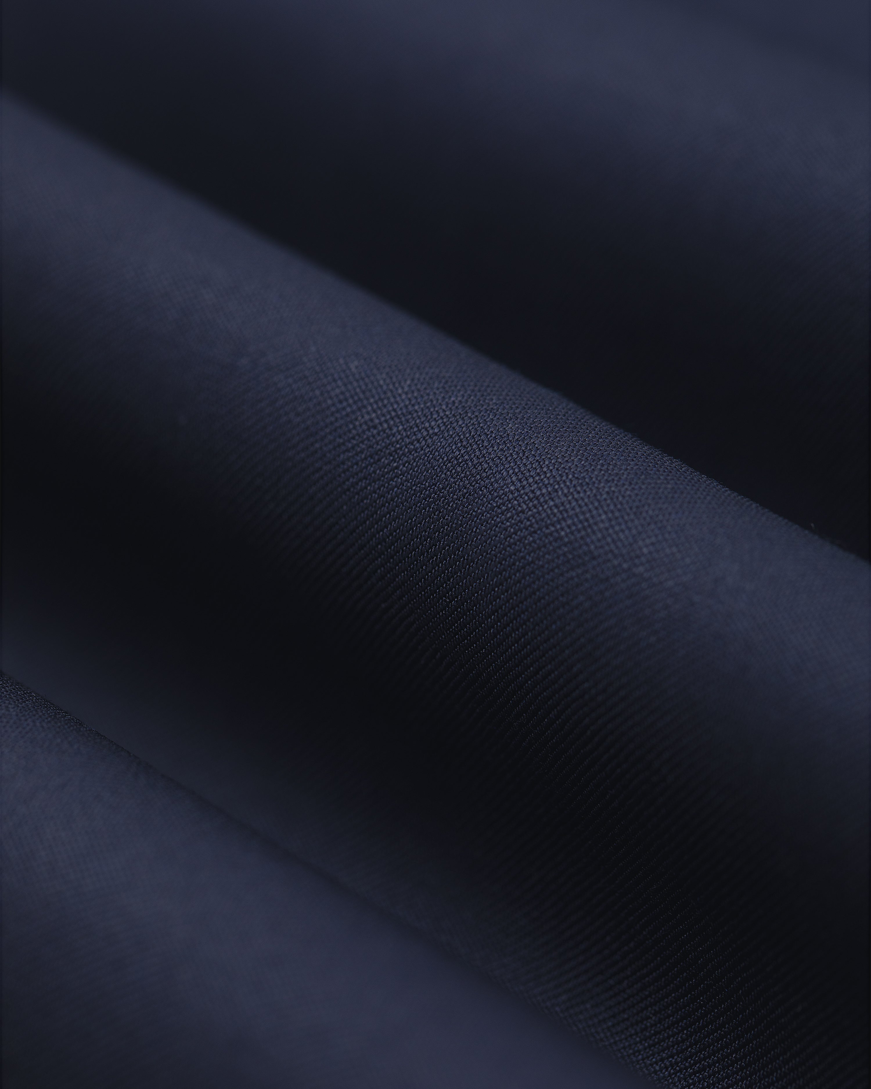 Close-up of Single-Pleated Gabardine Trouser in dark navy, showing diagonal ridges and softly lit texture.