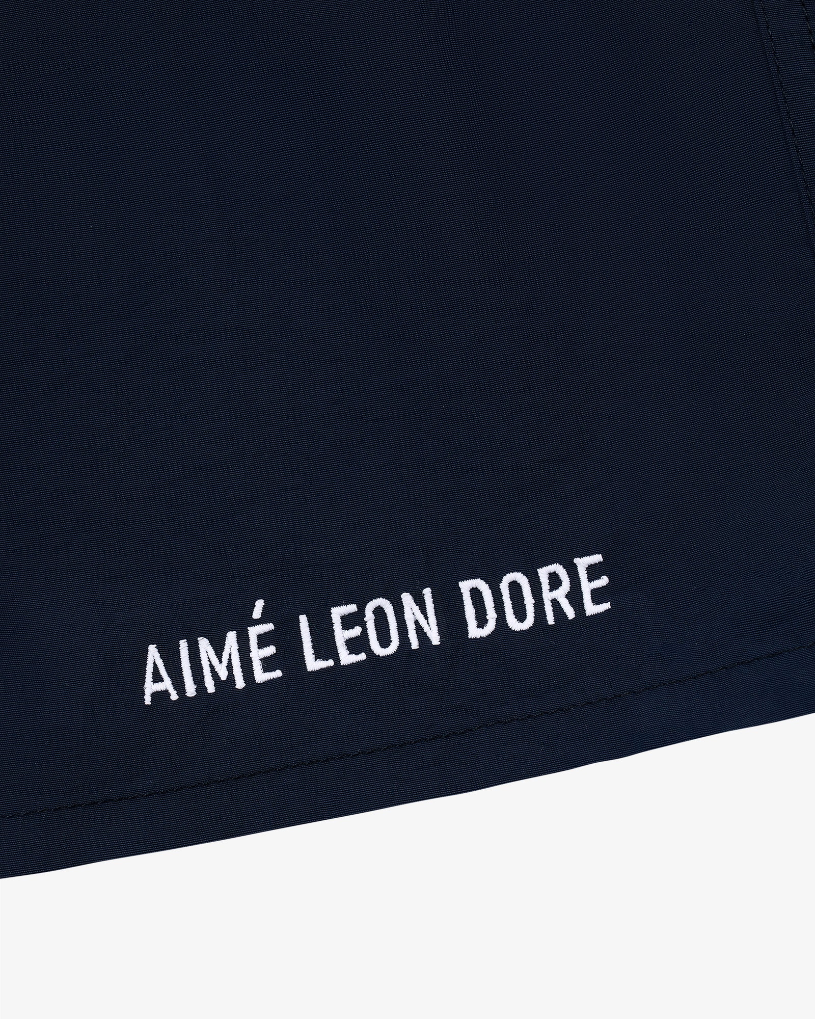 Close-up of Core Nylon Short in navy blue with AIMÉ LEON DORE embroidered in white near the hem.