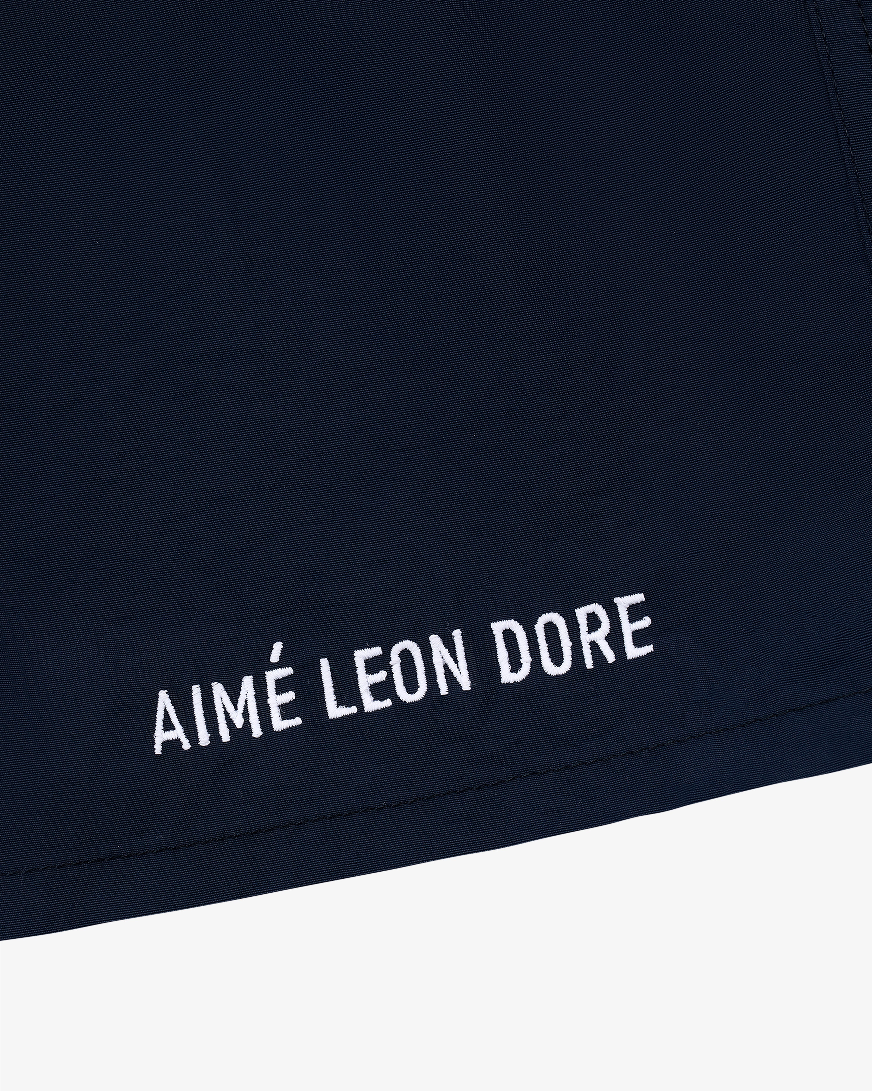 Close-up of Core Nylon Short in navy blue with AIMÉ LEON DORE embroidered in white near the hem.