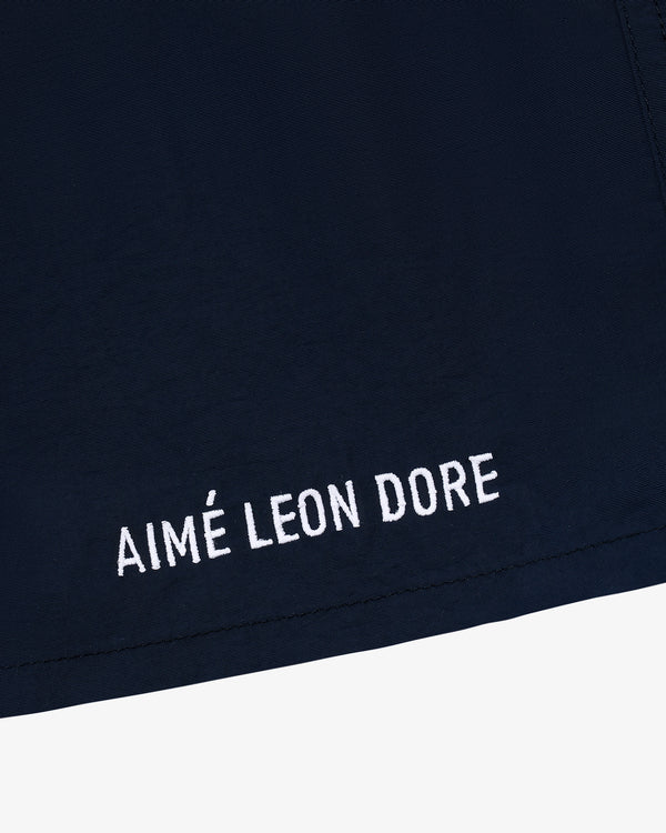 Close-up of Core Nylon Short in navy blue with AIMÉ LEON DORE embroidered in white near the hem.