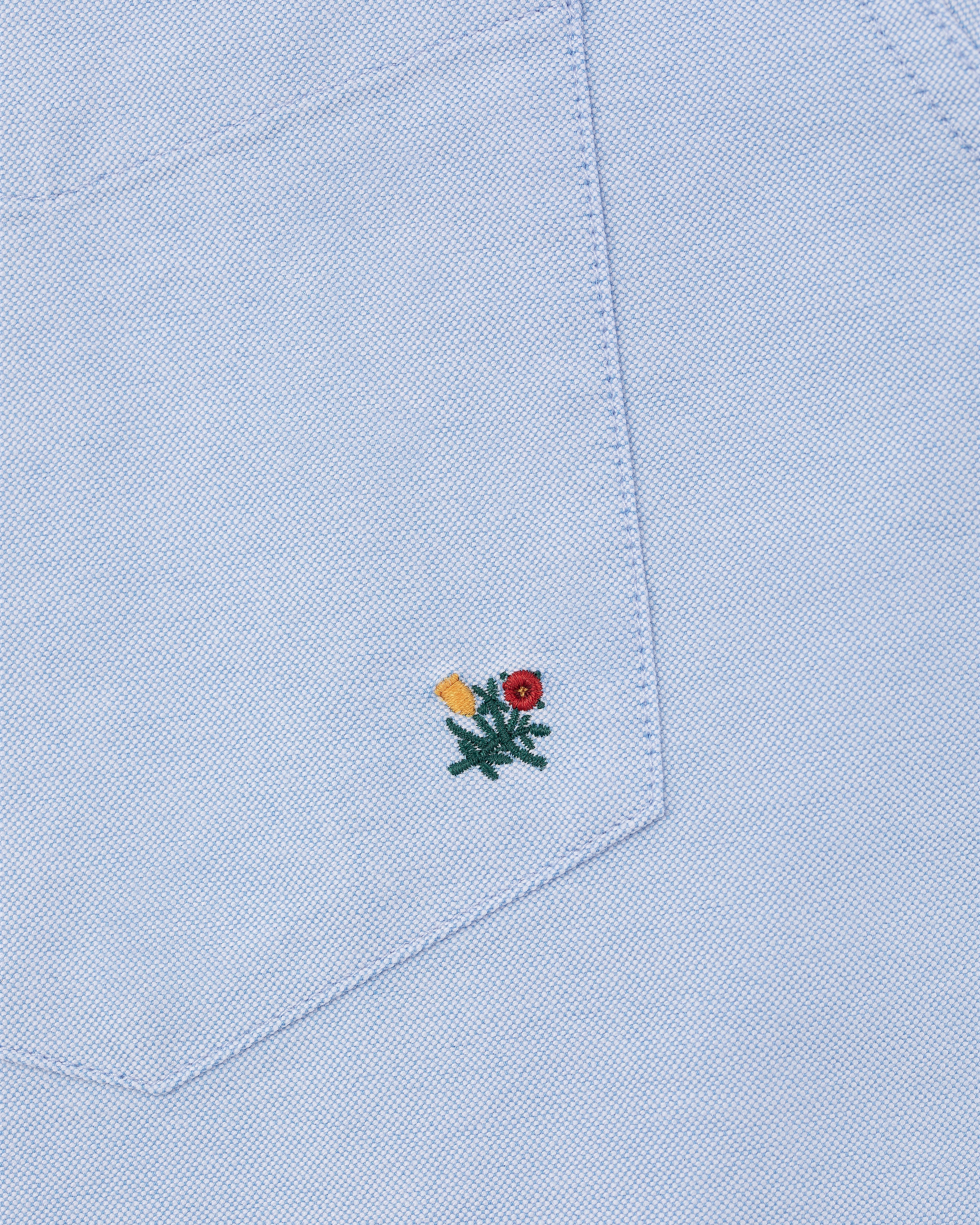 Light blue Crest Oxford Shirt with a fabric pocket featuring a small red and yellow flower embroidered near the bottom.