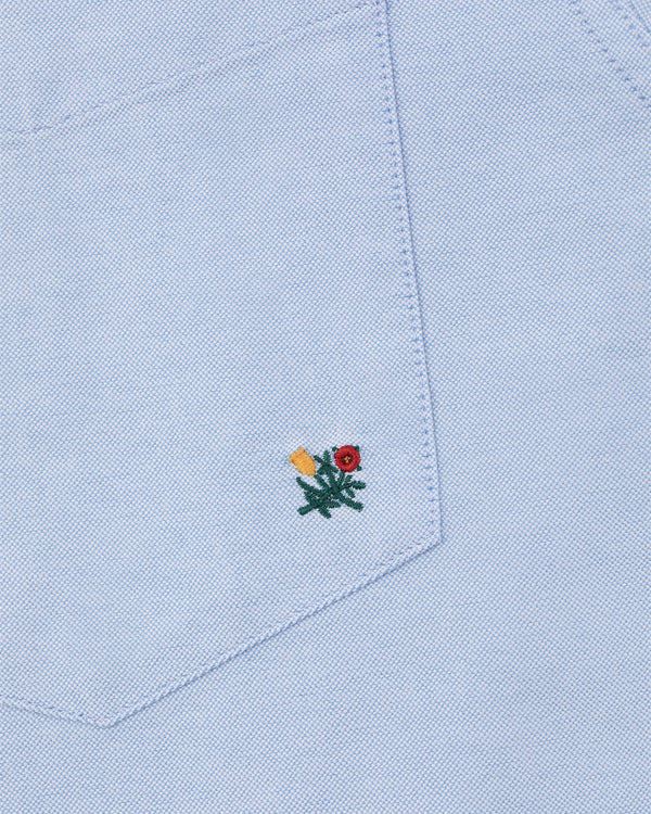 Light blue Crest Oxford Shirt with a fabric pocket featuring a small red and yellow flower embroidered near the bottom.