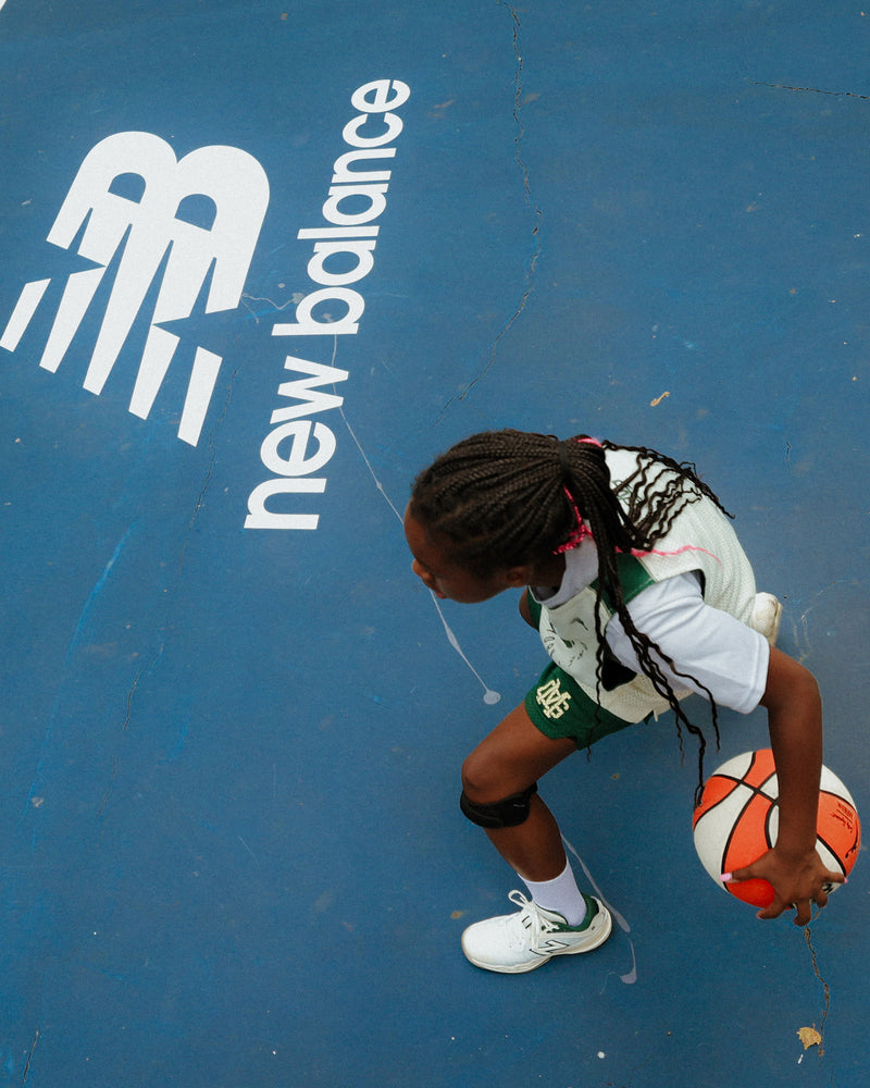 Person playing basketball on a court with New Balance branding