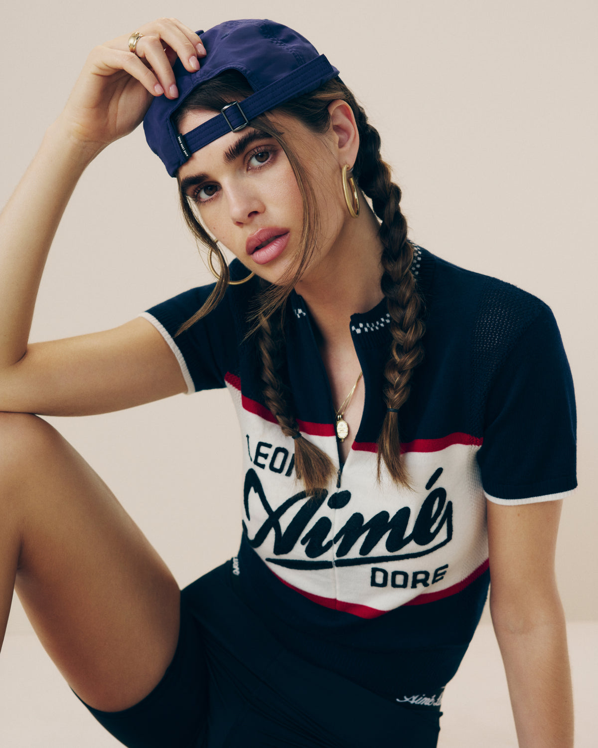Woman with two braids wears a backward purple cap and Merino Wool Cycling Jersey, sitting in a relaxed pose.