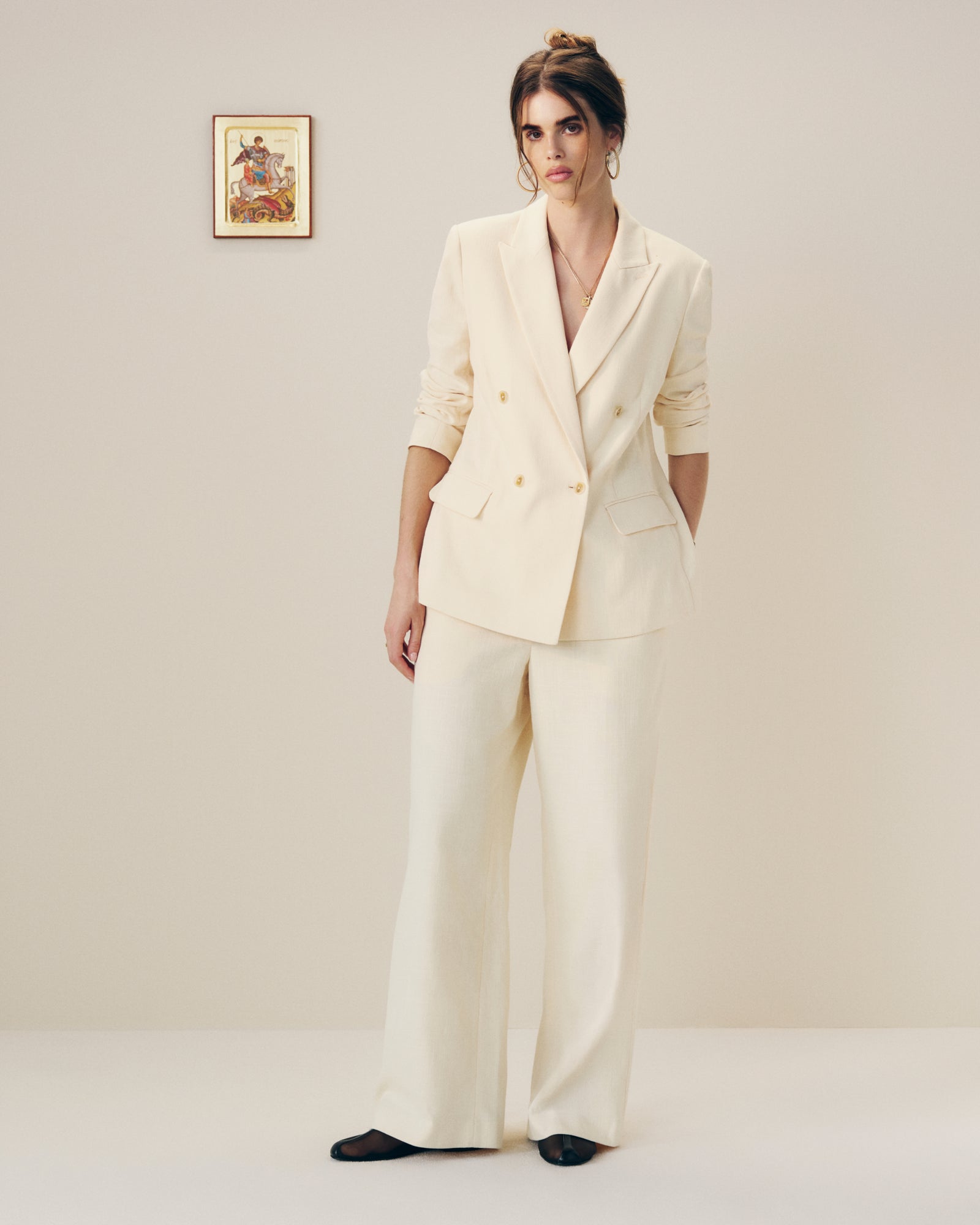 Woman wears a Double-Breasted Unconstructed Blazer indoors, hands in pockets, with framed art on the wall behind her.