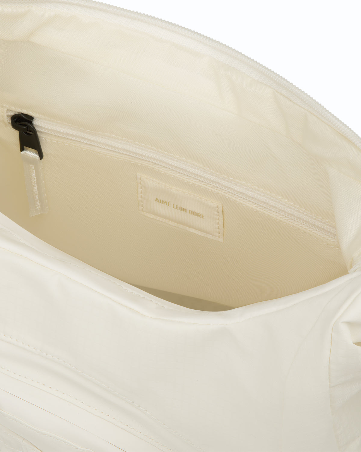 Close-up of the Nylon Messenger Bag's interior, showing a zip pocket and an AIME LEON DORE fabric label.