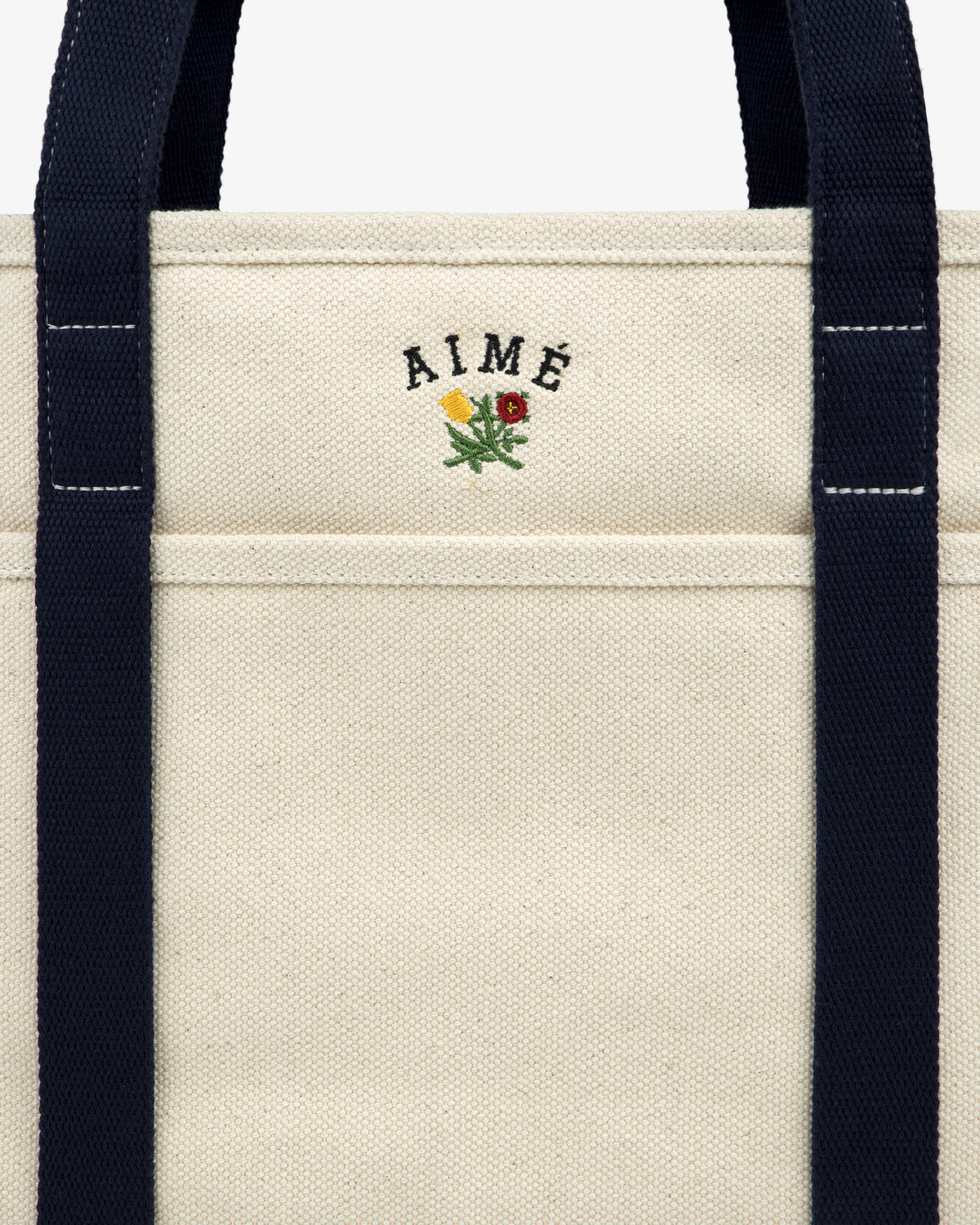 Small Crest Contrast Tote Bag: Cream canvas with navy straps, AIMÉ text, and a yellow-red embroidered flower.