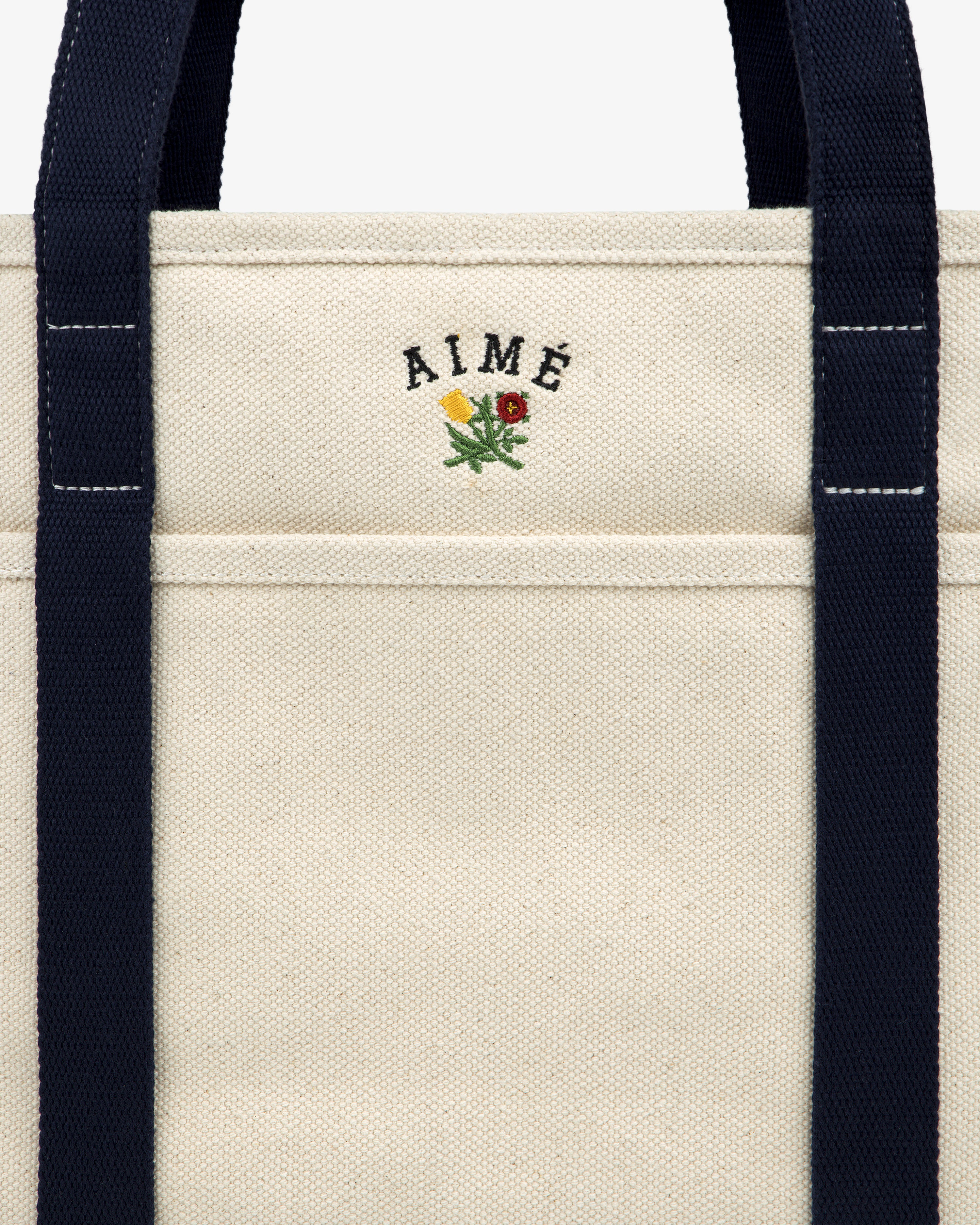 Small Crest Contrast Tote Bag: Cream canvas with navy straps, AIMÉ text, and a yellow-red embroidered flower.