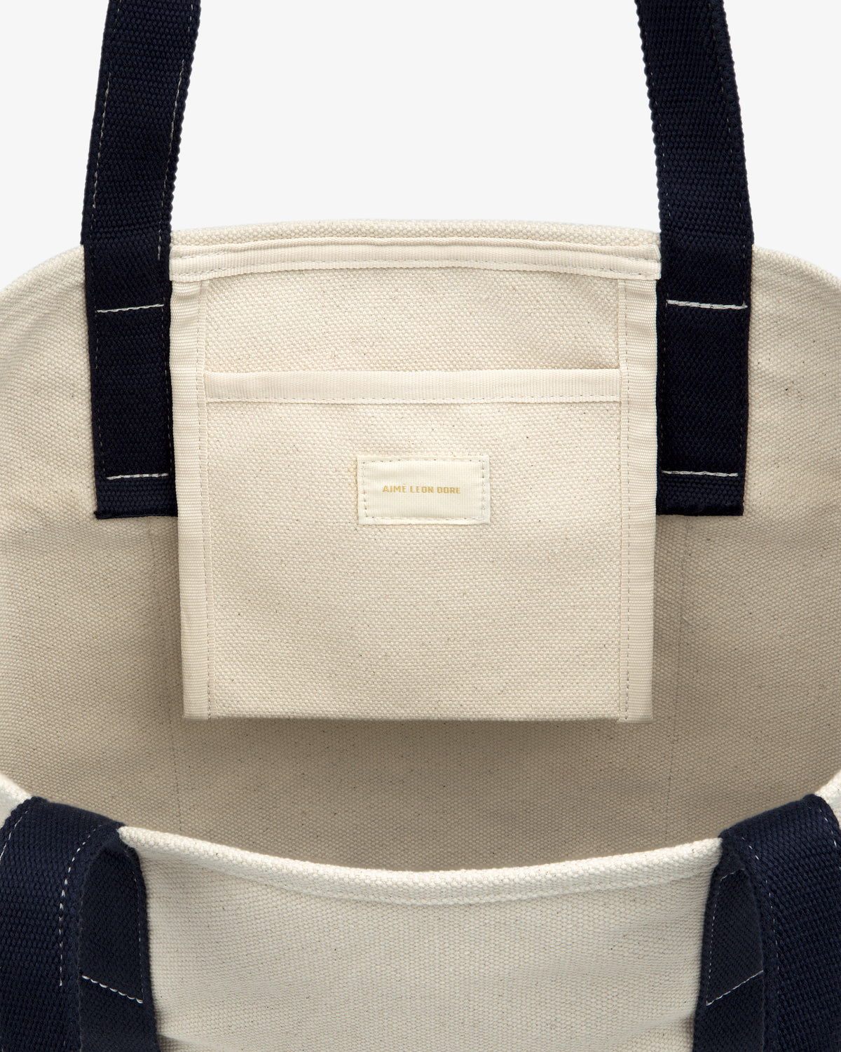 Large Crest Contrast Tote Bag in beige canvas with navy handles, inner pocket, and label on the pocket.