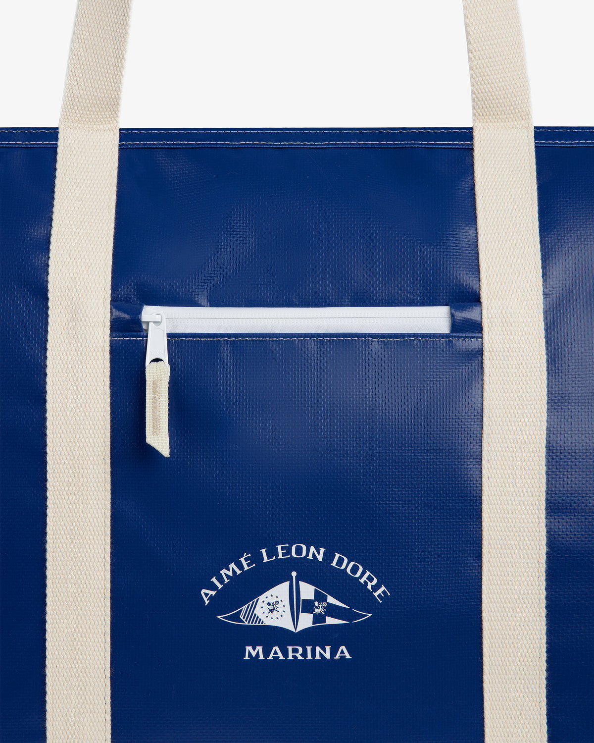 Carryall Marina Tote: Blue bag with white handles, front zip pocket, Aimé Leon Dore Marina text, and flag graphic.