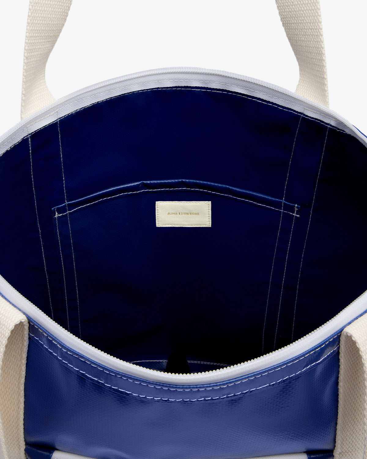 Carryall Marina Tote: Open blue bag with white handles, navy interior, and a small labeled inner pocket.