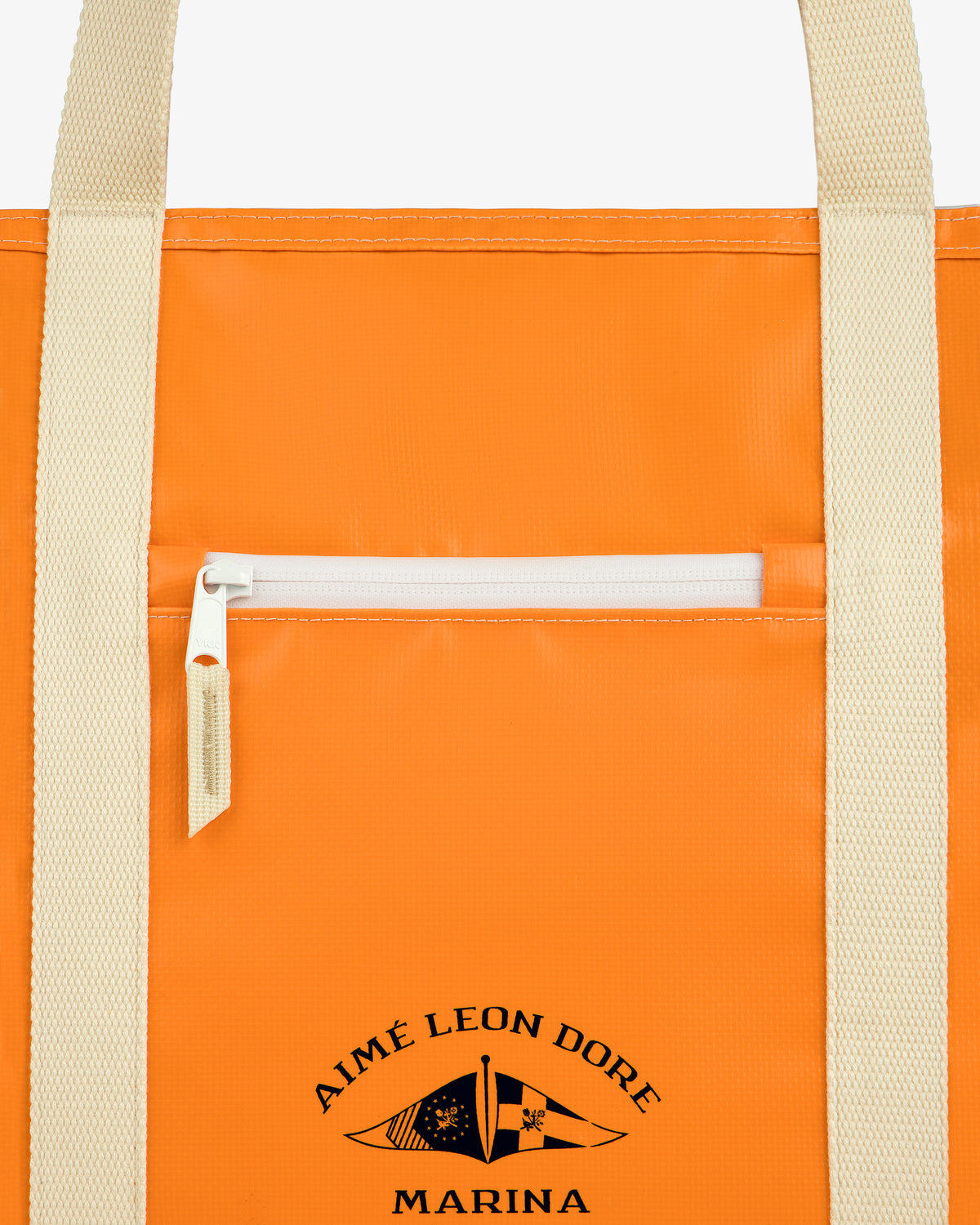Close-up of the Carryall Marina Tote, an orange bag with beige handles, front pocket, and AIMÉ LEON DORE MARINA logo.
