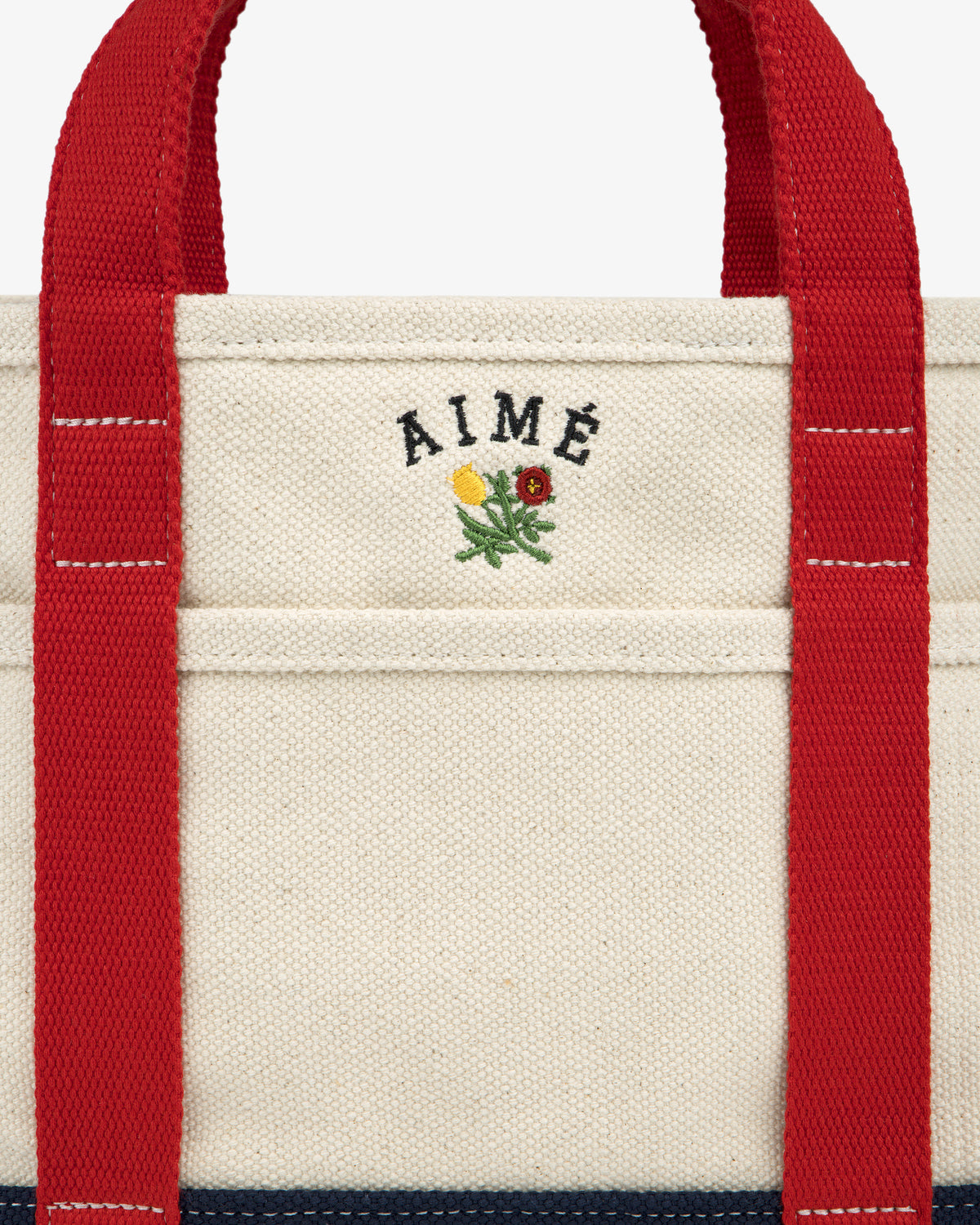 Mini Crest Contrast Tote Bag: cream canvas with red handles, AIMÉ text, and a flower above the front pocket.