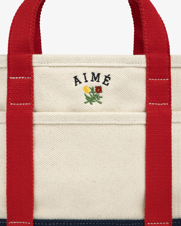 Mini Crest Contrast Tote Bag: cream canvas with red handles, AIMÉ text, and a flower above the front pocket.