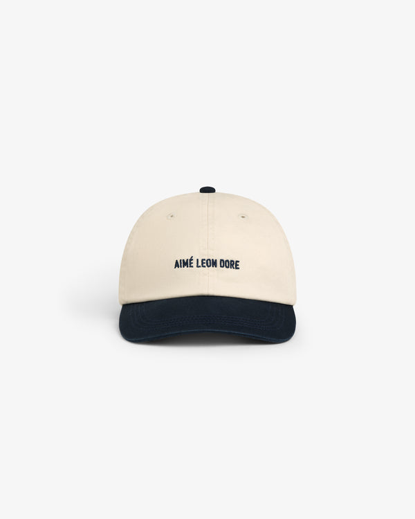 Washed Chino Hat in beige with AIMÉ LEON DORE text on front and dark blue brim, shown on a white background.