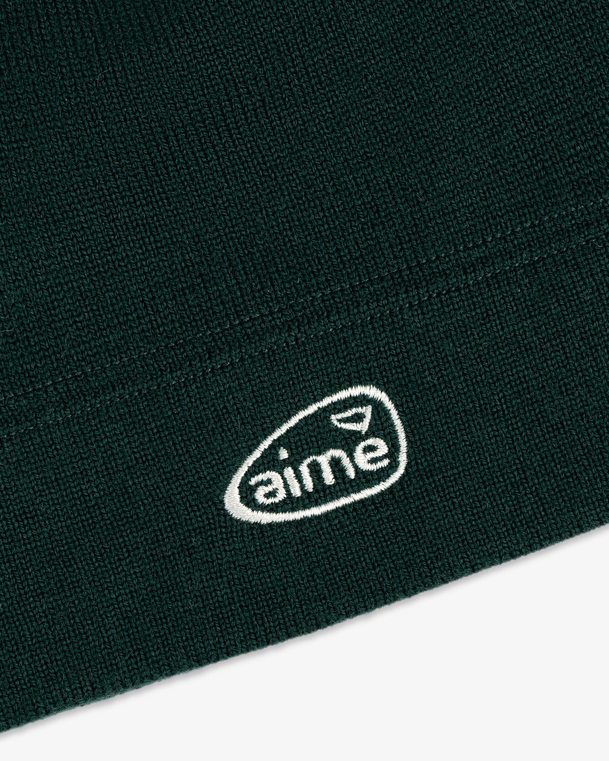 Close-up of the ALD Golf Skull Cap featuring dark green knit fabric and a white oval aime logo embroidery.