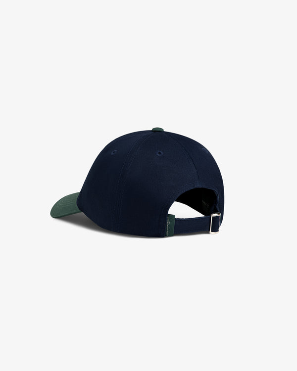 The ALD Golf Logo Hat in navy blue features a green brim, adjustable strap, and metal buckle at the back.