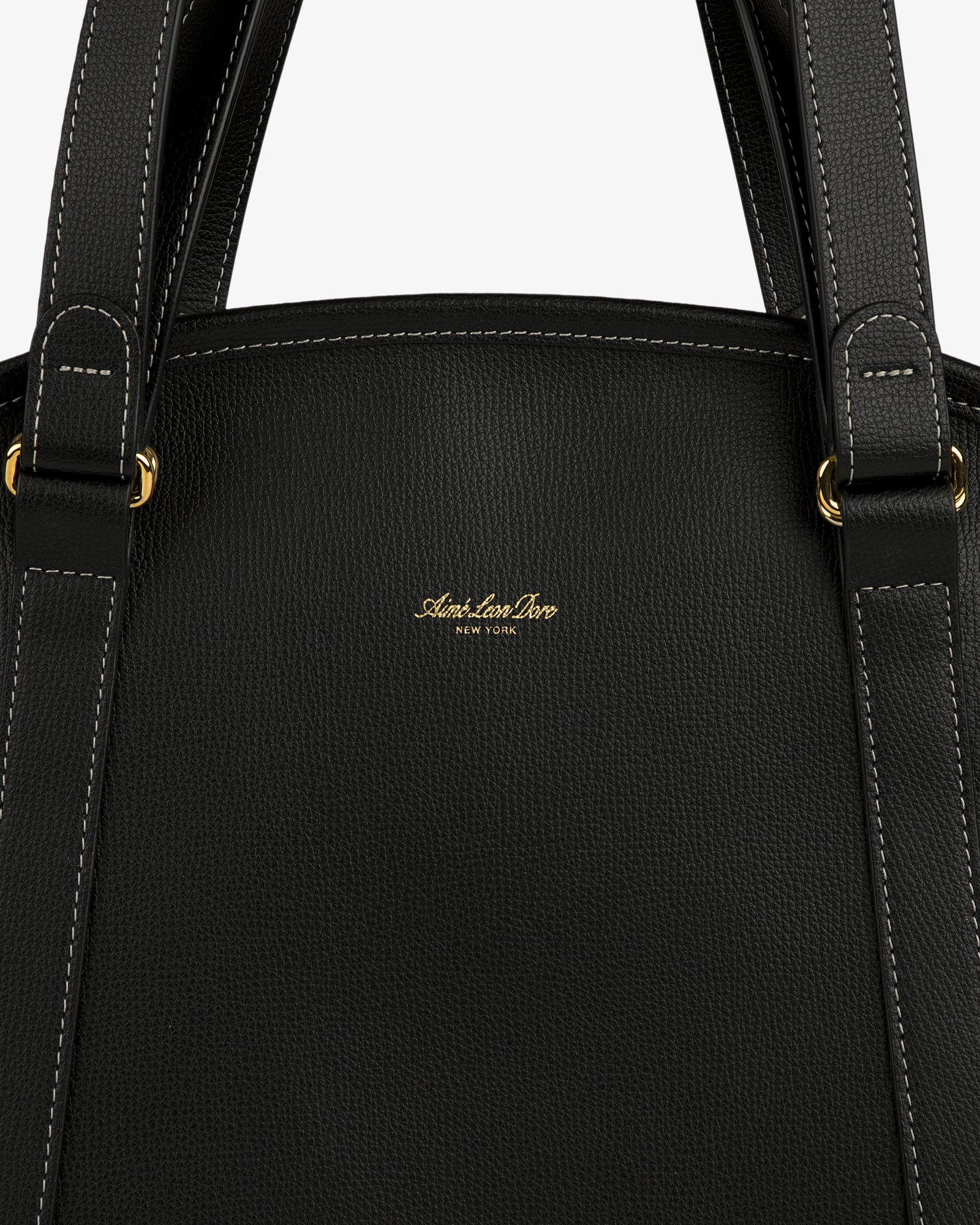 Close-up of the Full Grain Leather Weekender Bag, black with white stitching, gold hardware, and a central gold logo.