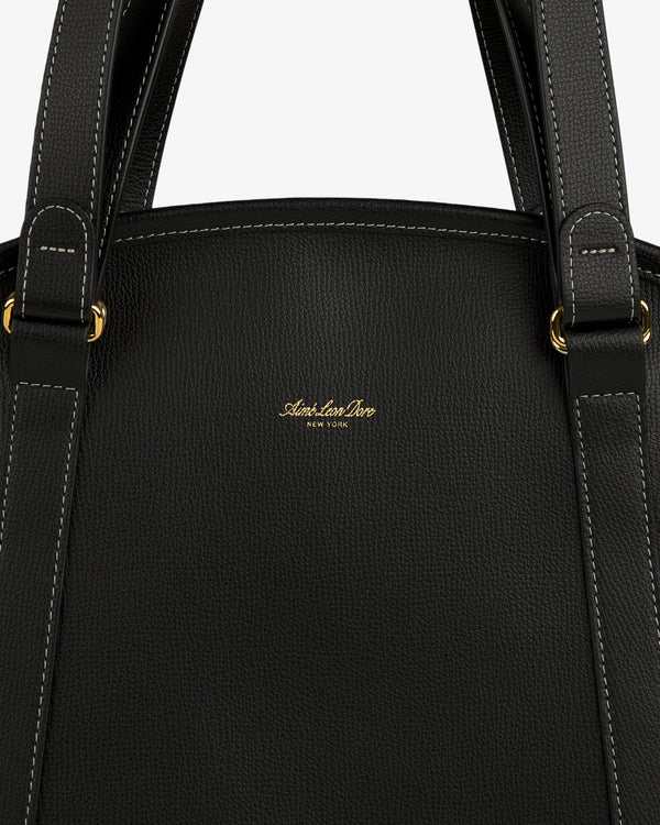 Close-up of the Full Grain Leather Weekender Bag, black with white stitching, gold hardware, and a central gold logo.