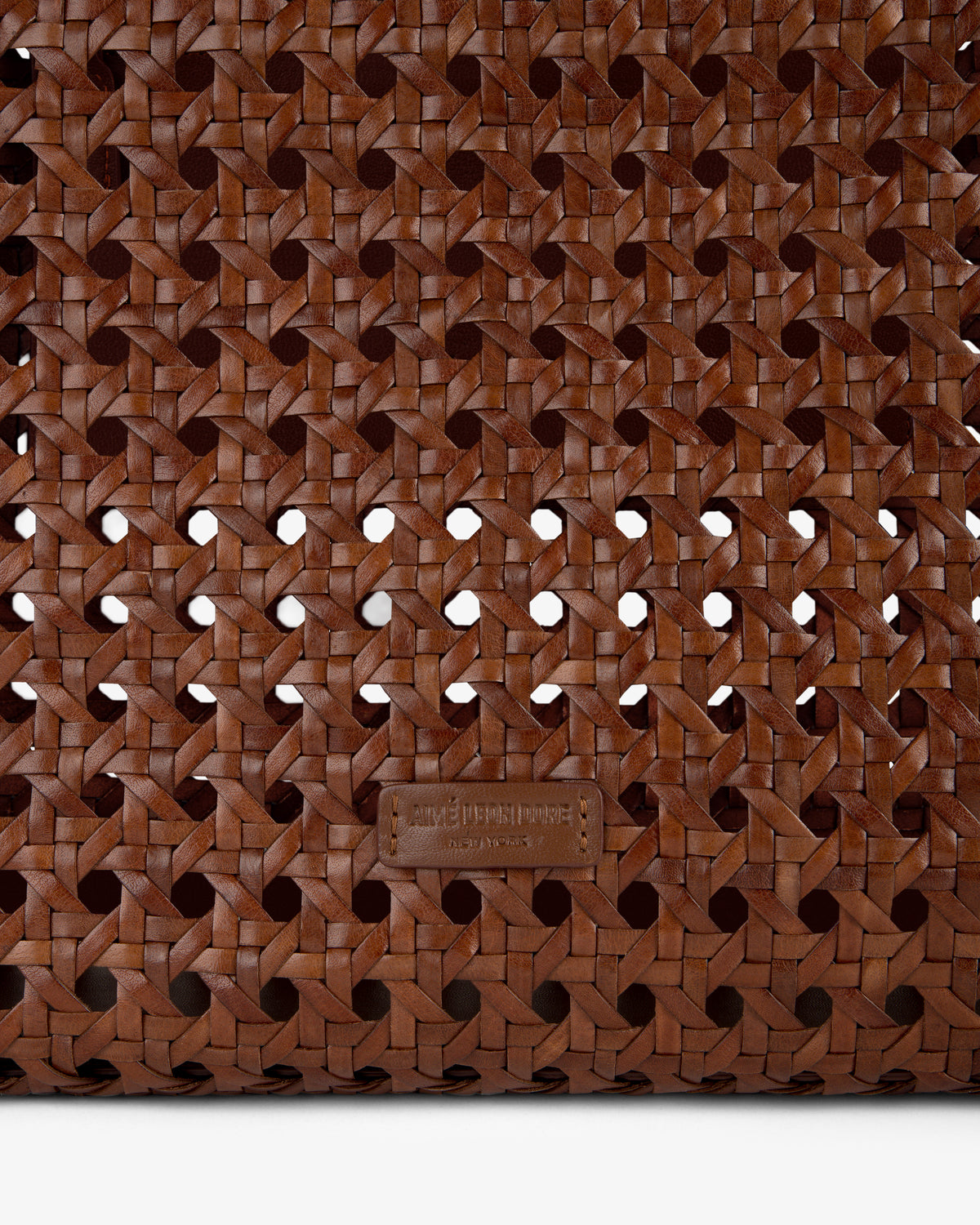 Close-up of the Woven Leather Tote Bag, featuring brown woven leather and a small rectangular label at the bottom center.