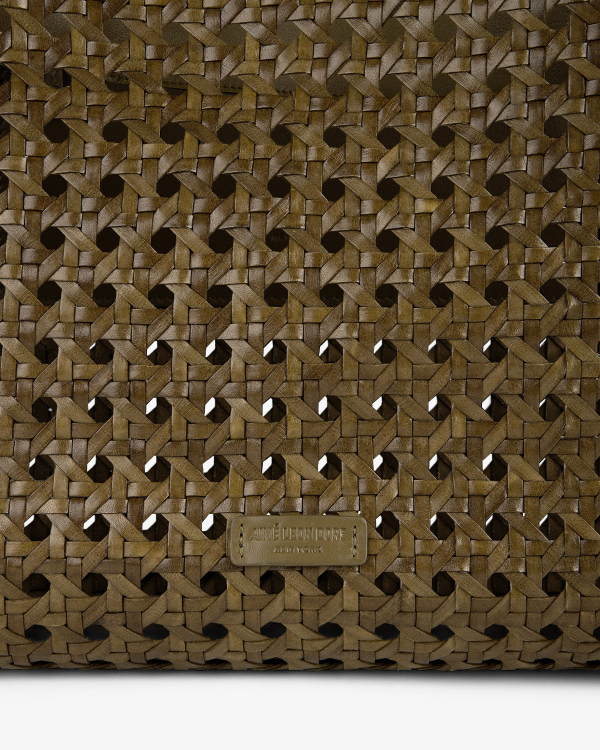 Close-up of the Woven Leather Tote Bag in brown with a small embossed rectangular label at the bottom center.