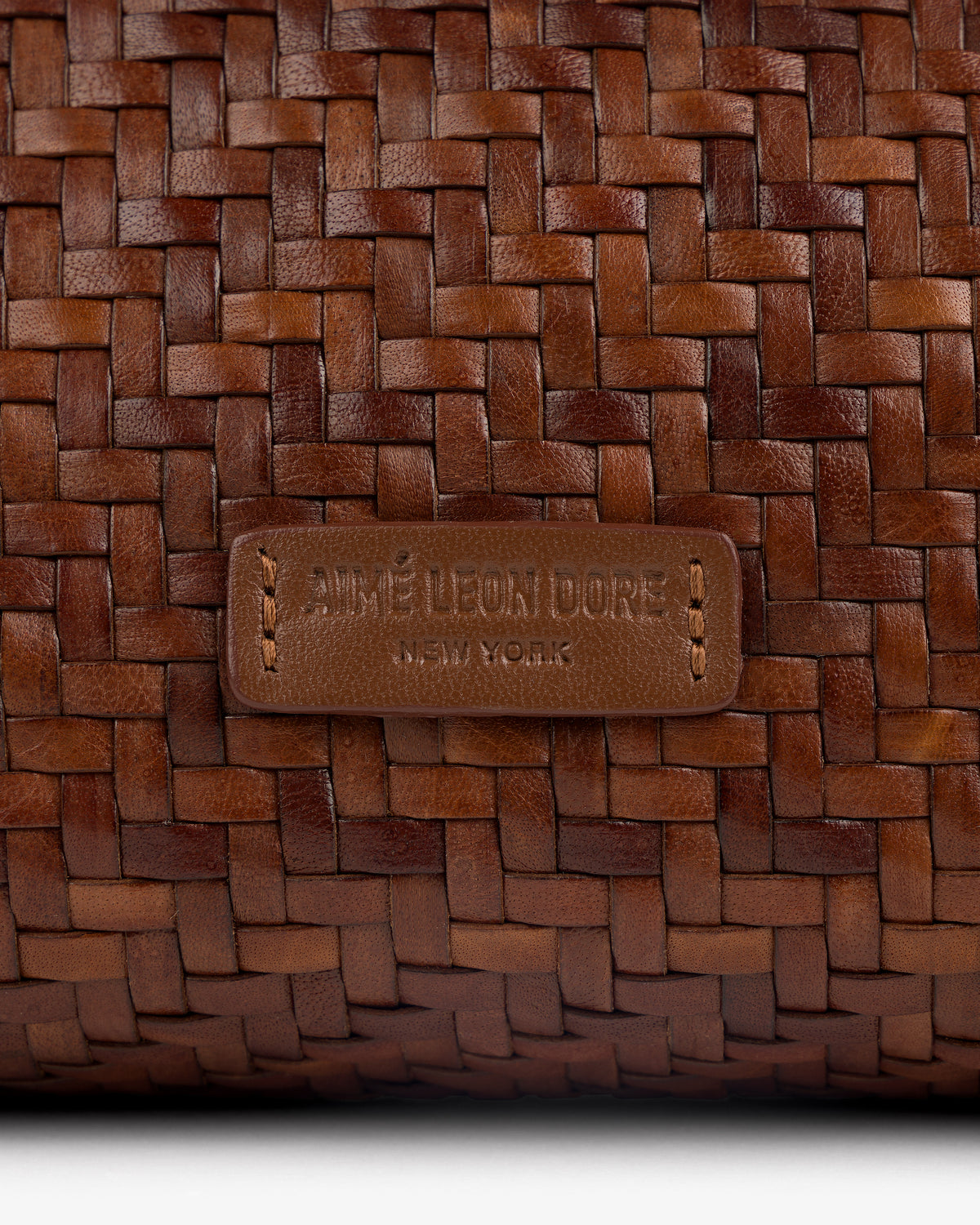 Close-up of the Woven Leather Shoulder Bag’s brown weave and stitched AIMÉ LEON DORE NEW YORK label.