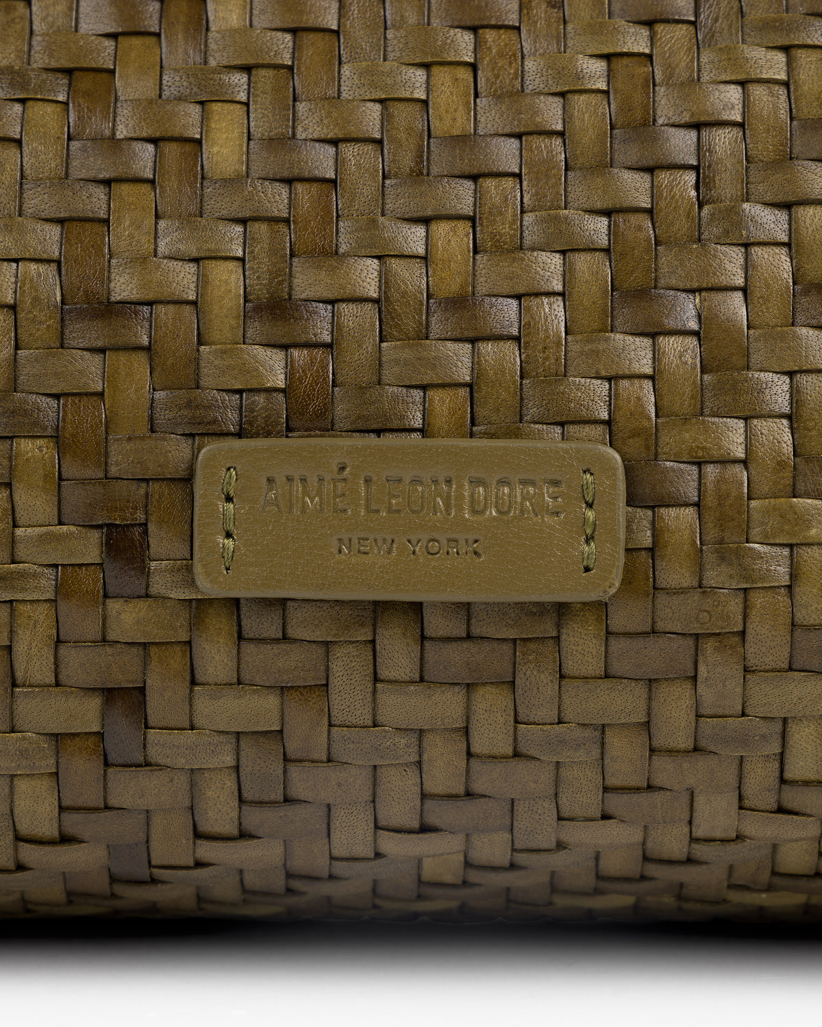 Close-up of a Woven Leather Shoulder Bag with an Aimé Leon Dore New York label stitched at the center.