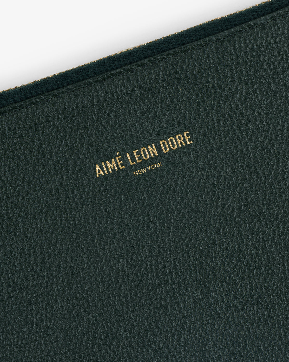 Close-up of the Large Leather Pouch’s textured dark green surface with Aimé Leon Dore New York in gold lettering.