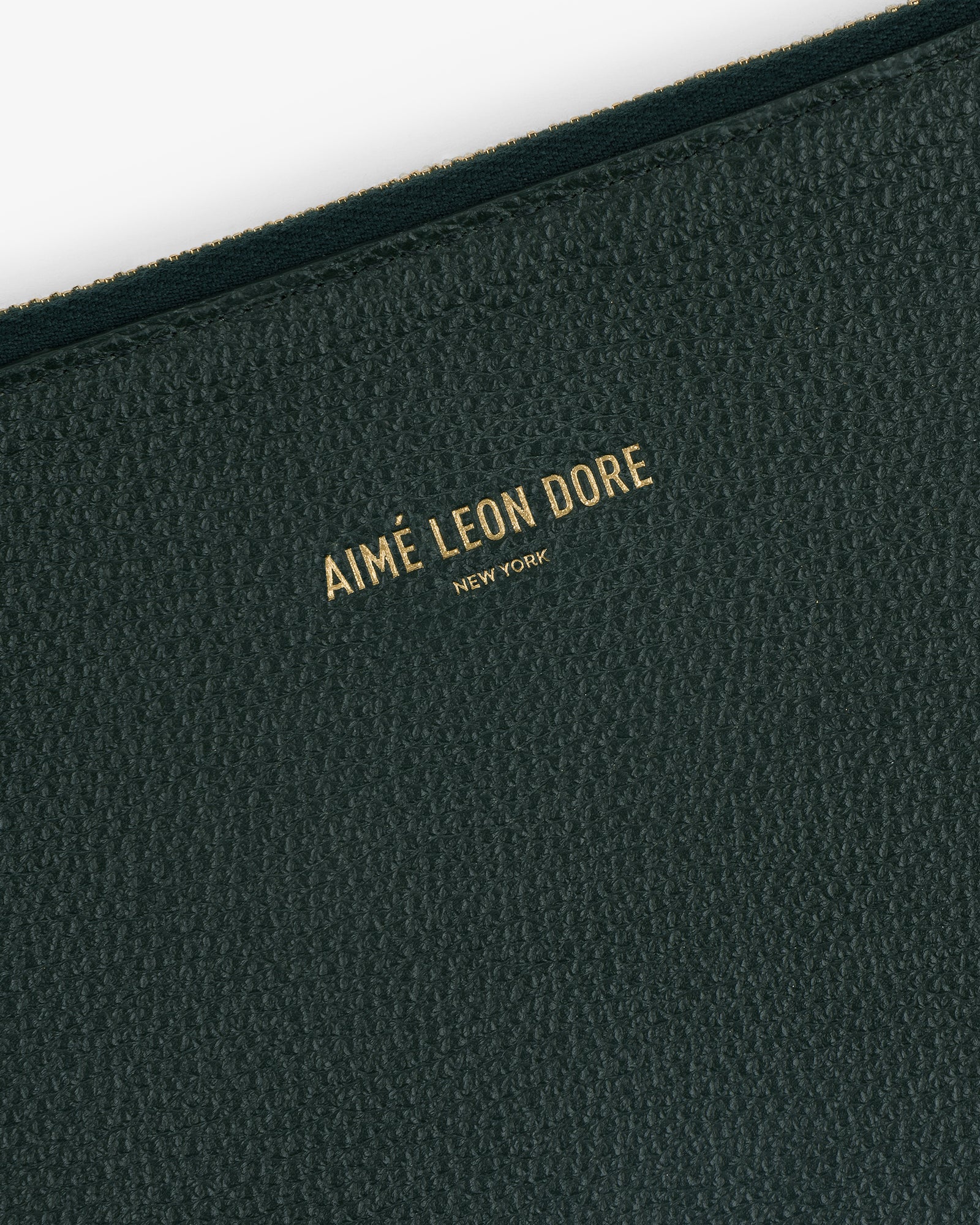 Close-up of the Large Leather Pouch’s textured dark green surface with Aimé Leon Dore New York in gold lettering.