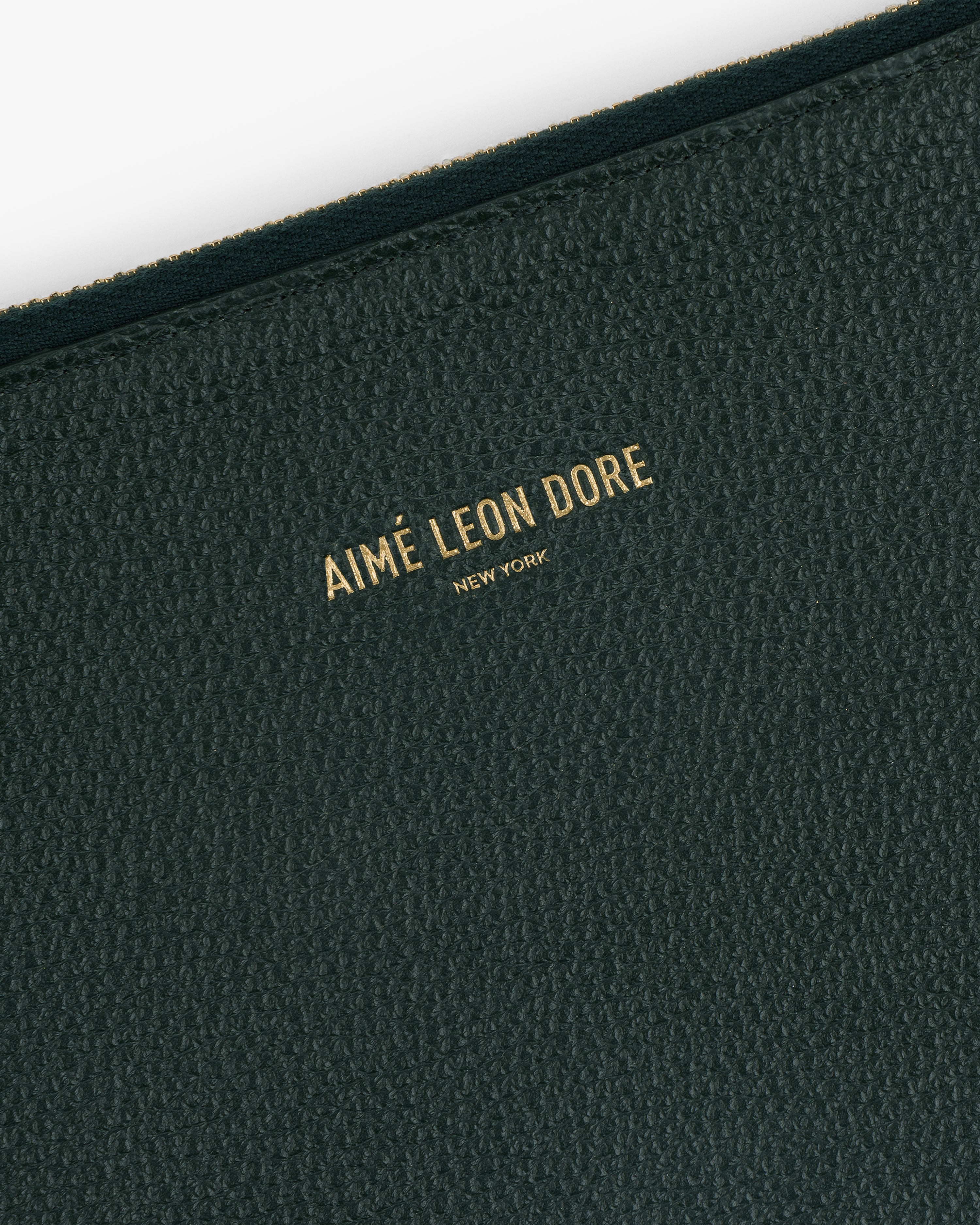 Close-up of the Large Leather Pouch’s textured dark green surface with Aimé Leon Dore New York in gold lettering.