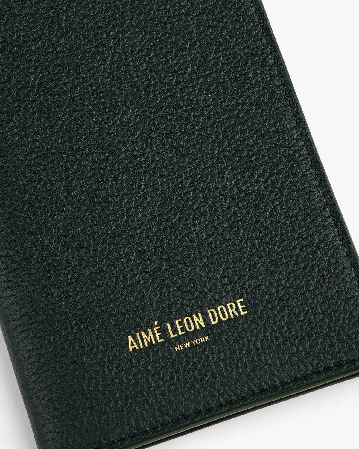 Close-up of a textured dark green Leather Passport Holder with AIMÉ LEON DORE NEW YORK in gold lettering.