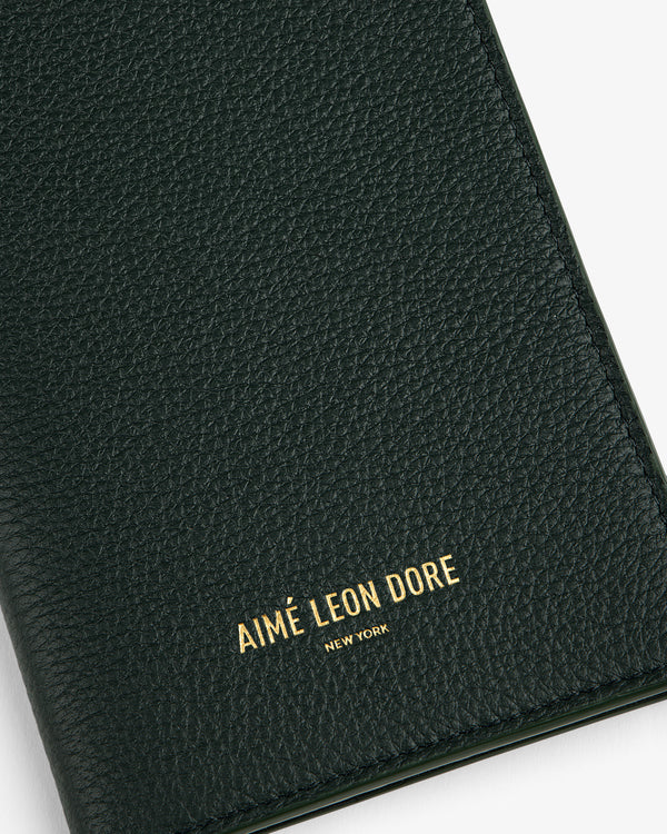 Close-up of a textured dark green Leather Passport Holder with AIMÉ LEON DORE NEW YORK in gold lettering.