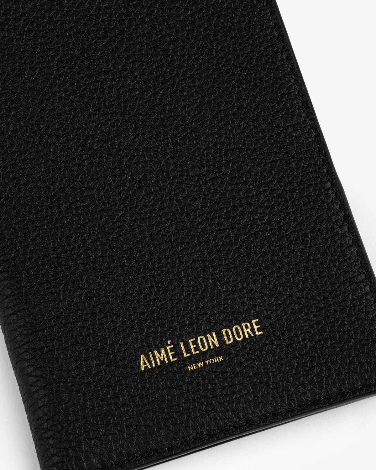 Black textured leather passport holder with AIMÉ LEON DORE NEW YORK embossed in gold letters on the front.