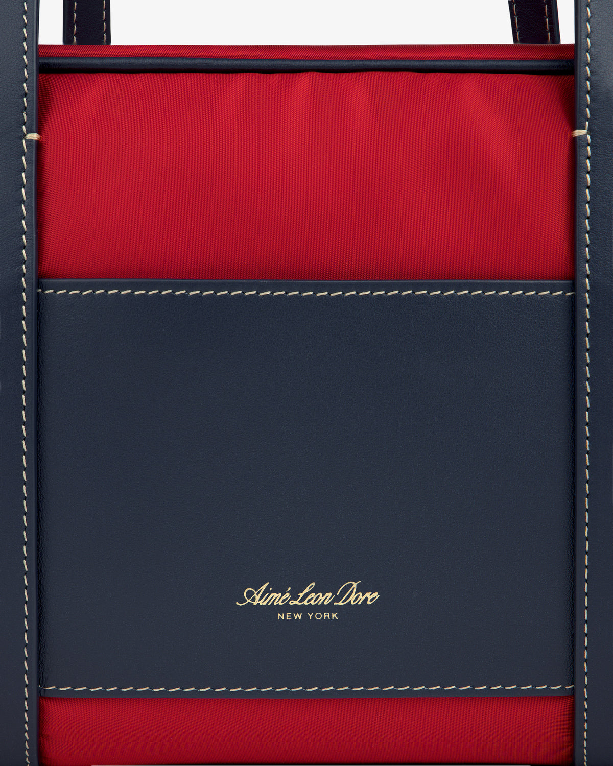Close-up of a red and navy Mini Duffle Shoulder Bag with white stitching and gold Aimé Leon Dore New York text.