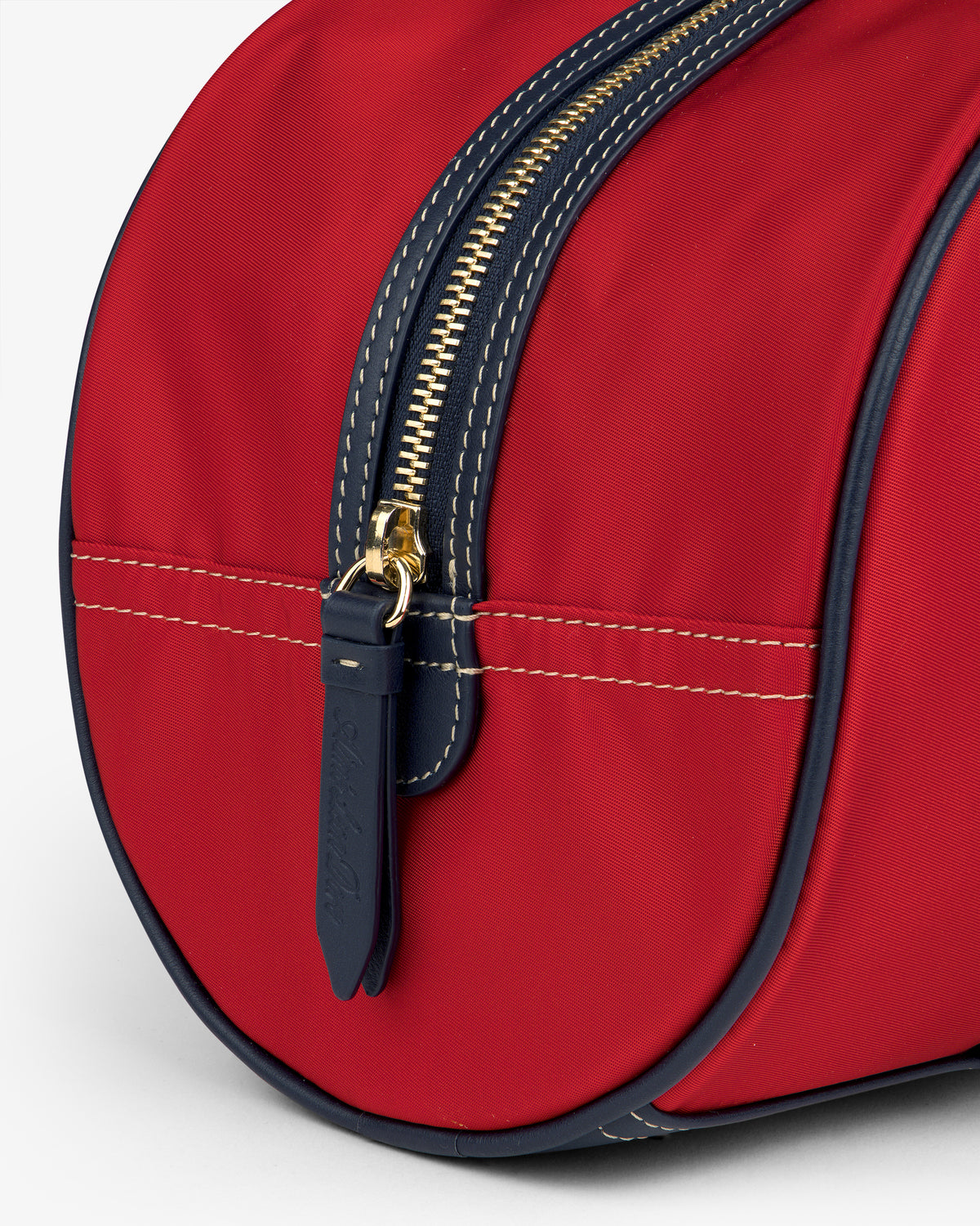 Close-up of the Mini Duffle Shoulder Bag: red with a gold zipper, navy trim, and white stitching on a light background.