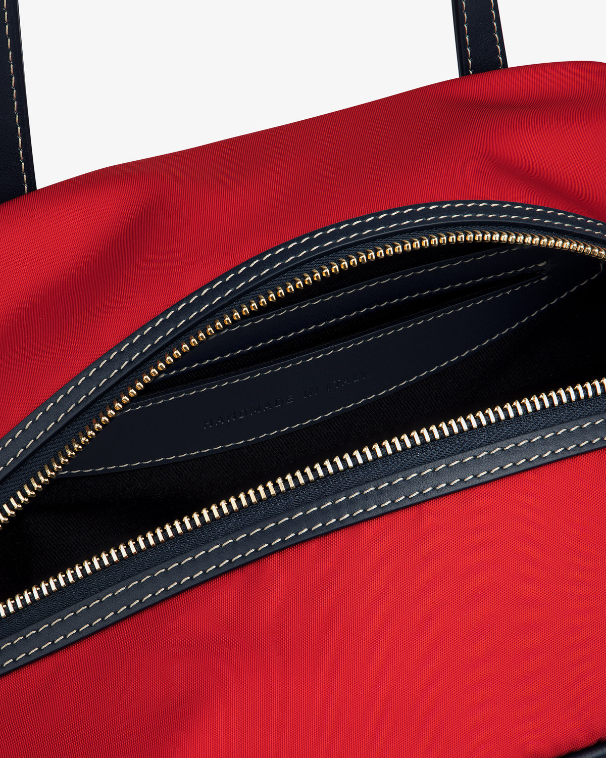 Close-up of Mini Duffle Shoulder Bag: open red design, gold zipper, black lining, and white stitched details.