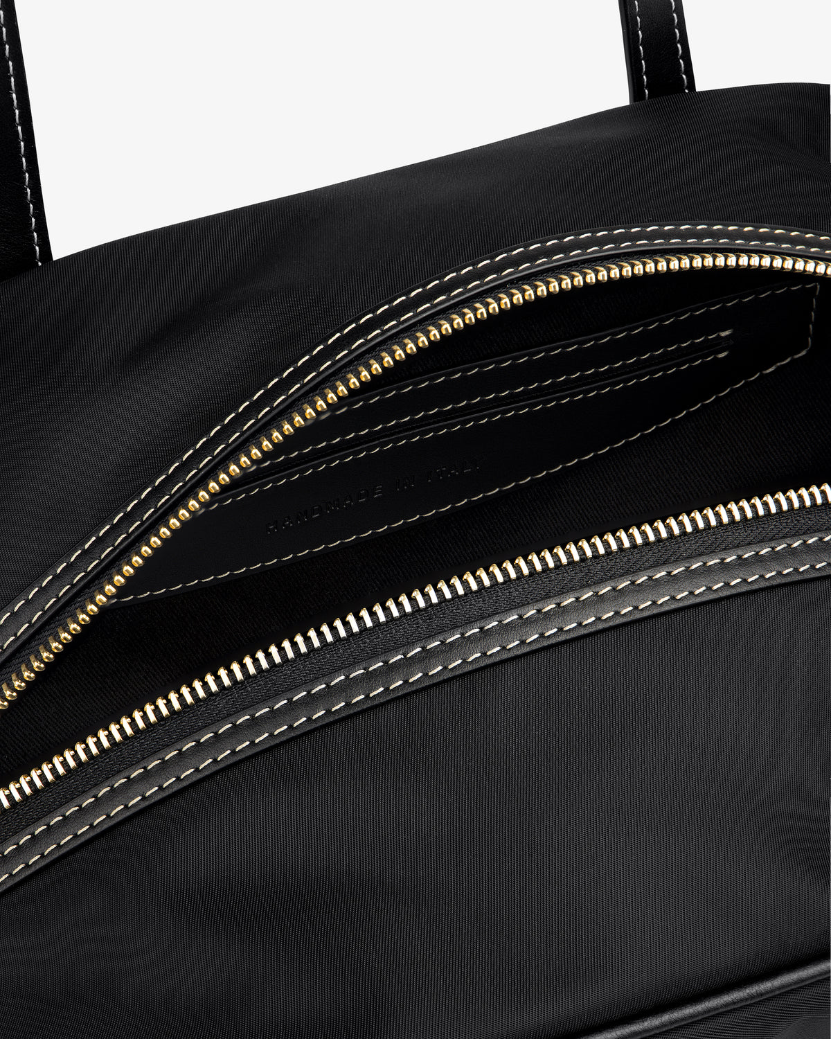 Close-up of the Mini Duffle Shoulder Bag in black with a gold zipper and white stitching, partially open to reveal interior.