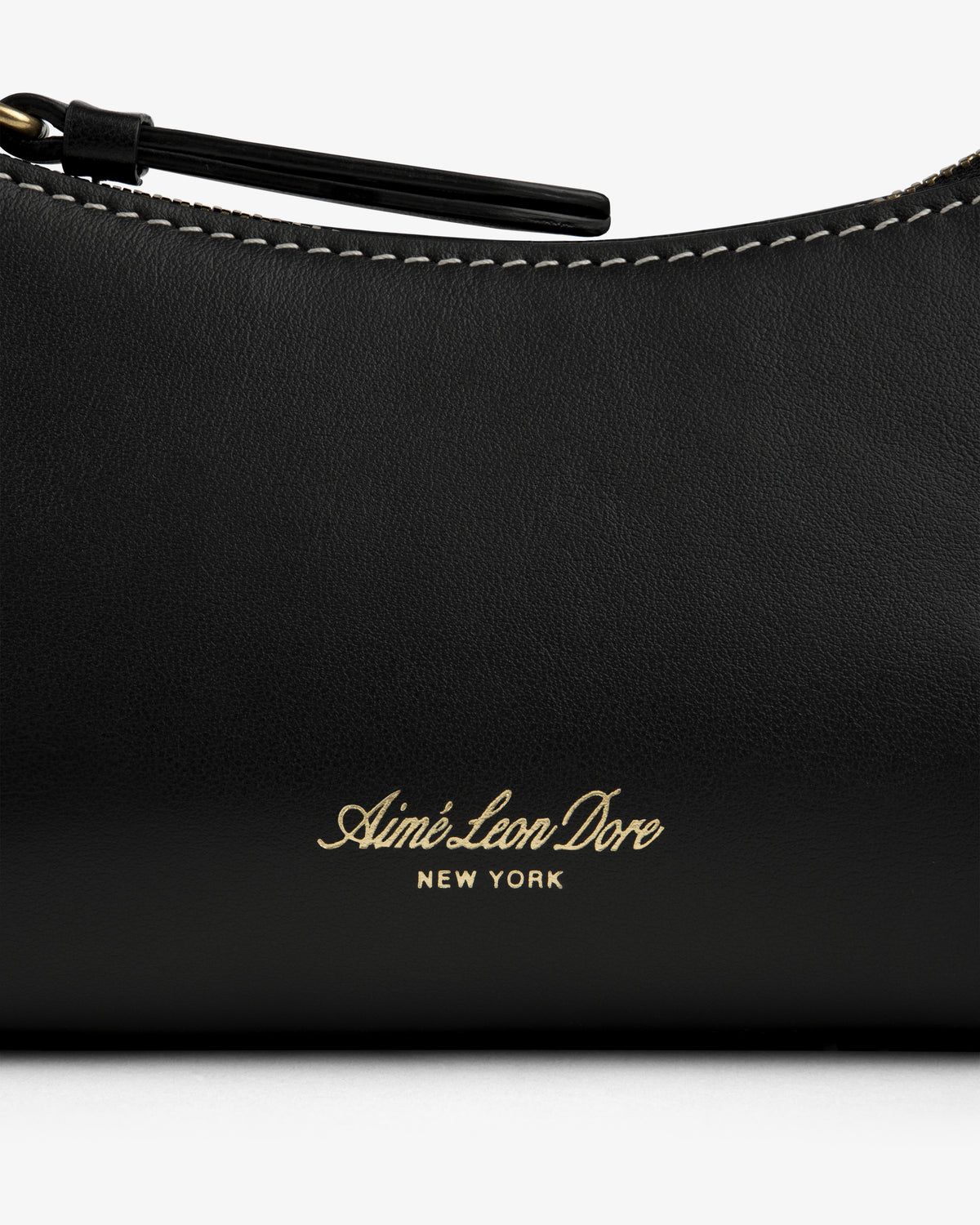 Close-up of the Convertible Leather Belt Bag in black leather with Aimé Leon Dore New York gold text and white stitching.