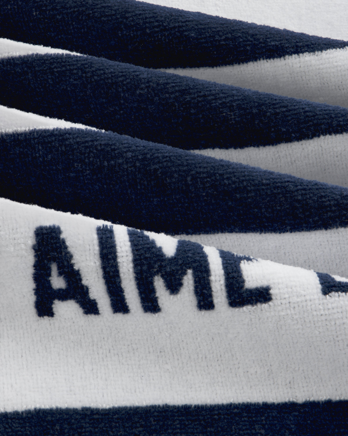 A close-up of the Striped Beach Towel shows soft navy and white stripes with bold navy text on the white stripe.
