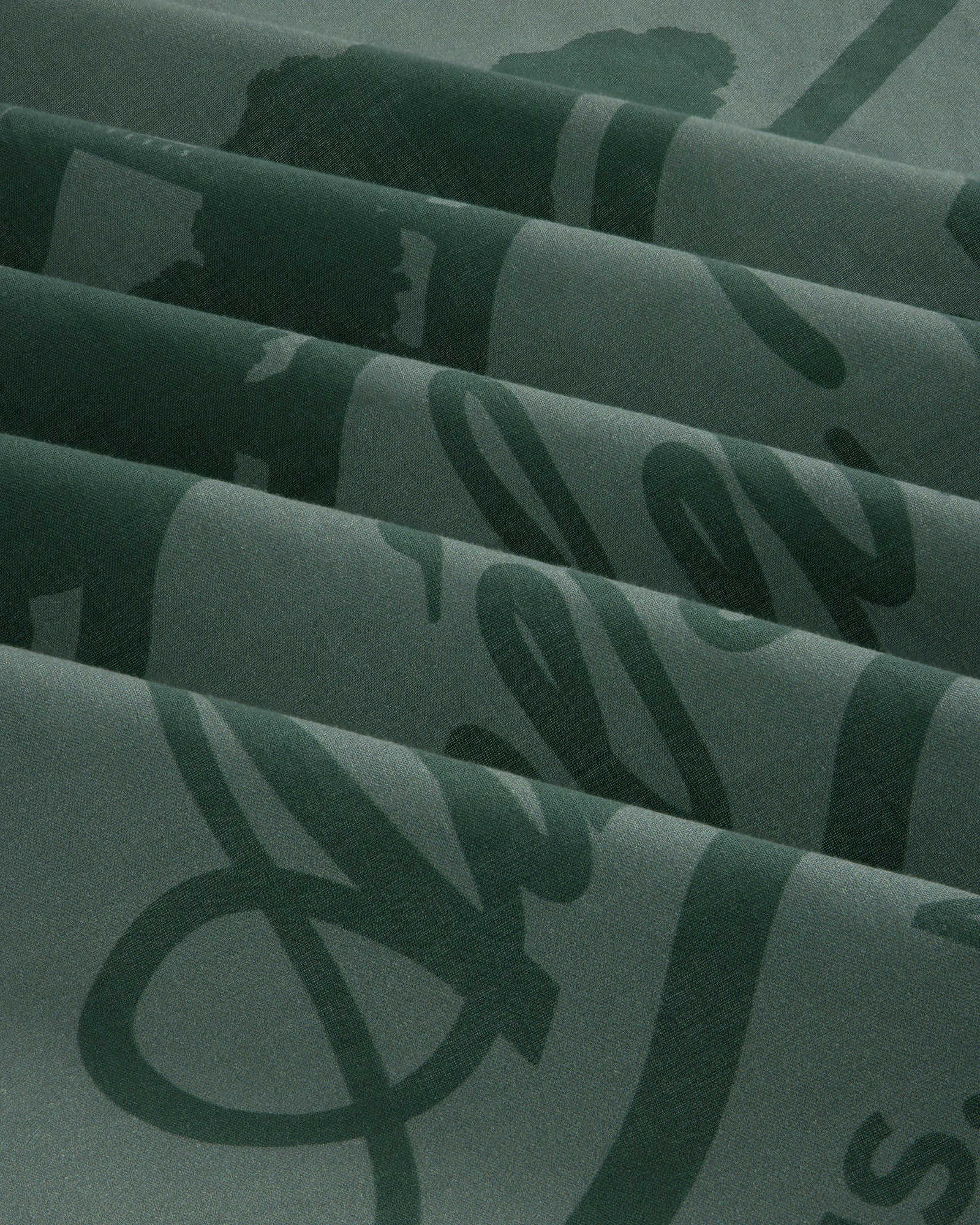 Sun Faded Unisphere Bandana in dark green with shiny cursive script, folded in neat pleats.