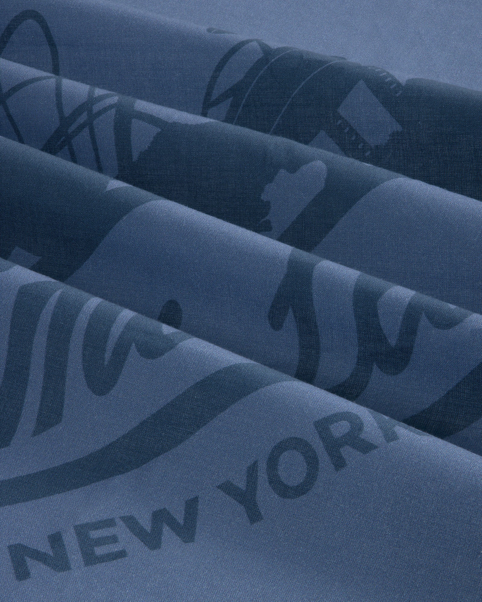 Close-up of folded Sun Faded Unisphere Bandana in blue with partial printed text, including “NEW YORK.”.