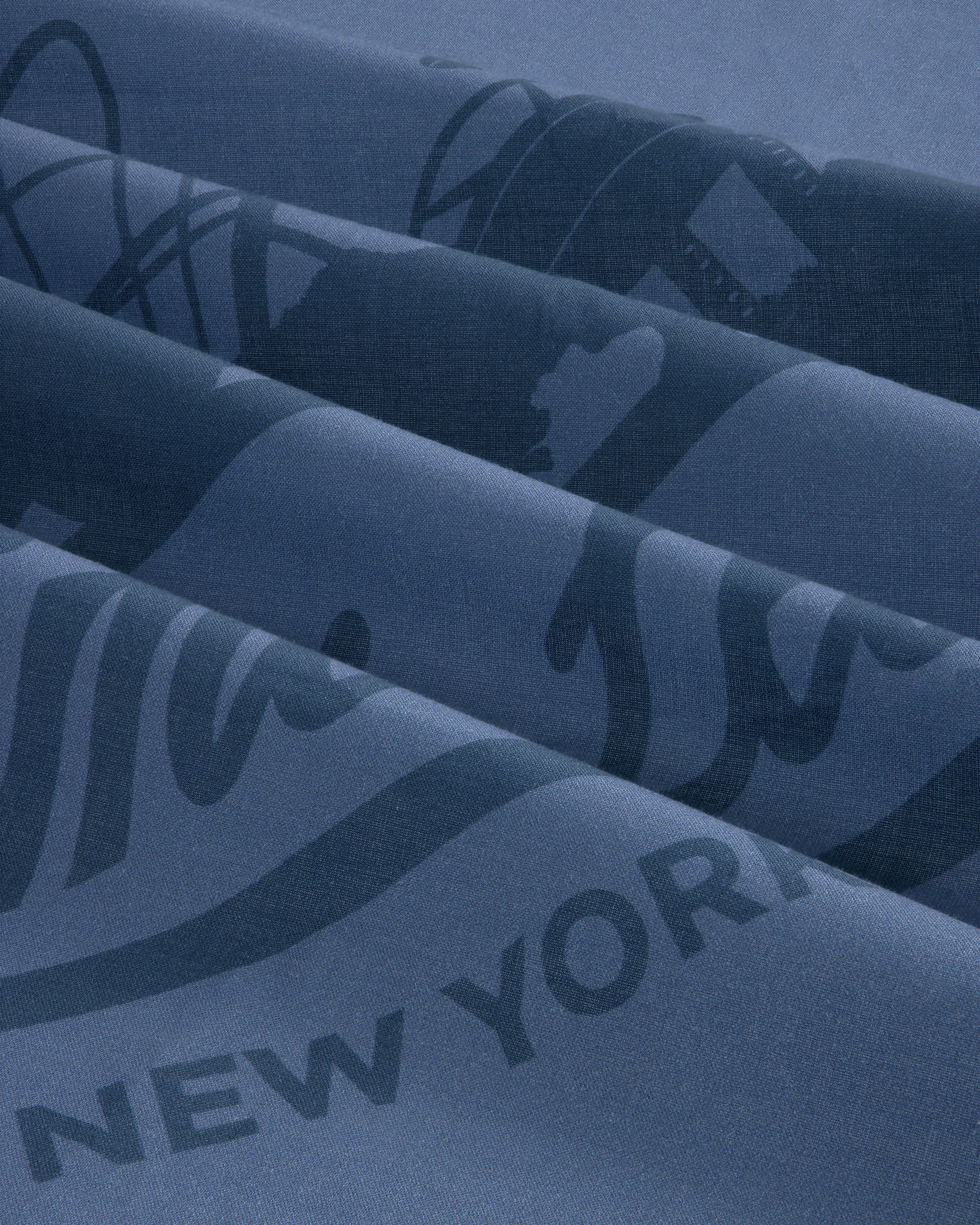 Close-up of folded Sun Faded Unisphere Bandana in blue with partial printed text, including “NEW YORK.”.