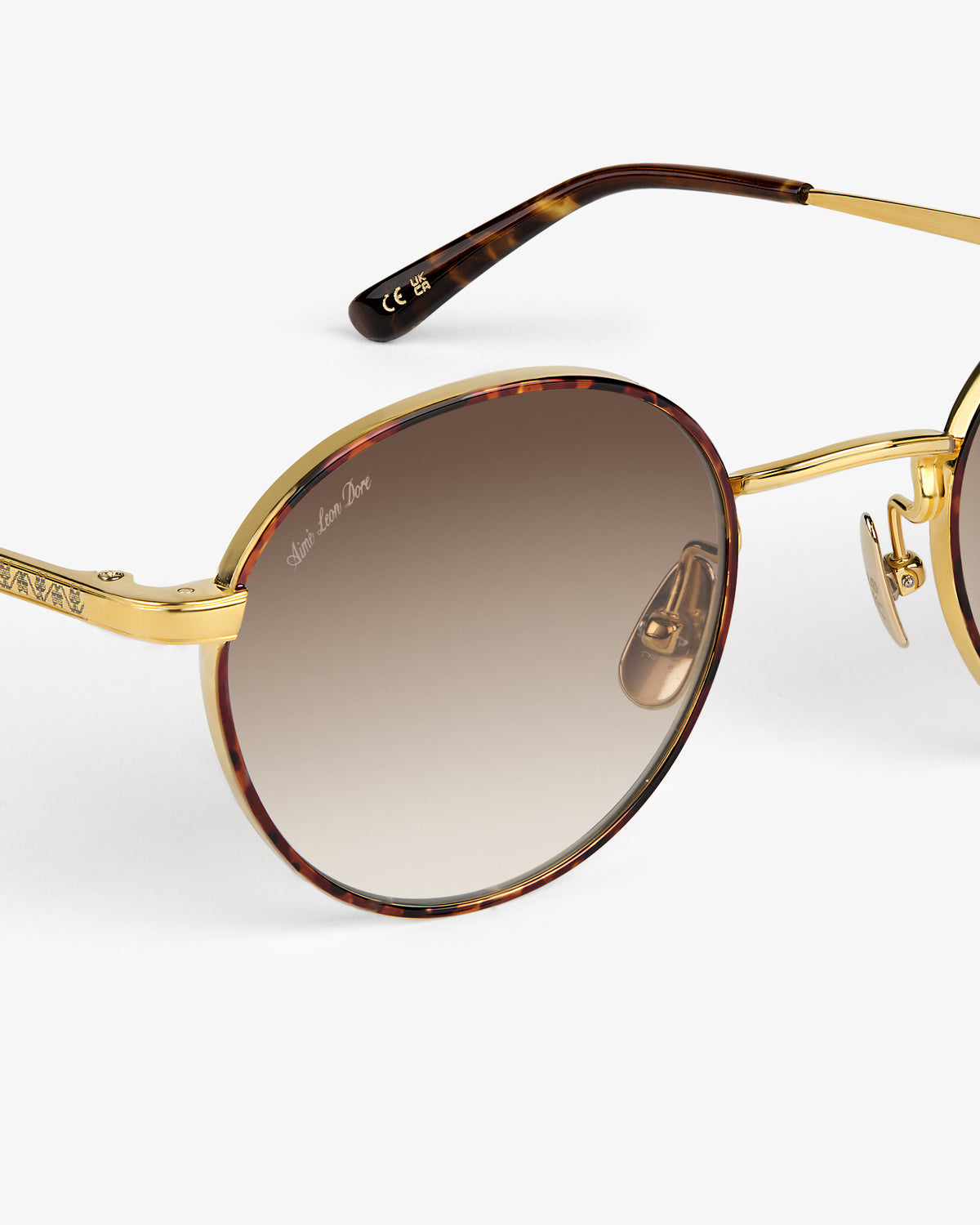 Giórgios Sunglasses: round gold frame, tortoiseshell rim, and brown gradient lenses shown in close-up detail.