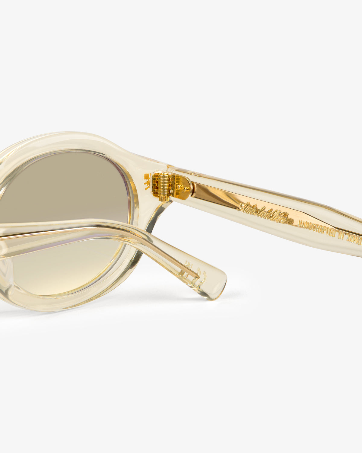 Close-up of Onásis Sunglasses—translucent beige with gold detailing and engraved arm—on a white background.