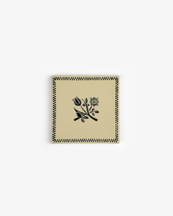 The Crest Coaster (Set of 4) features square beige ceramic pieces with black floral and checkered designs.