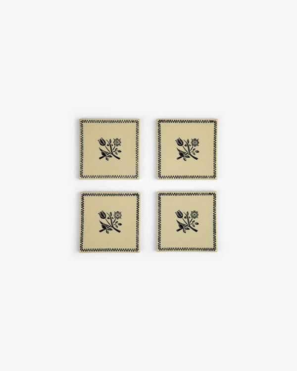 The Crest Coaster Set (4 pcs) features beige coasters with black floral designs and zigzag borders, arranged in a grid.