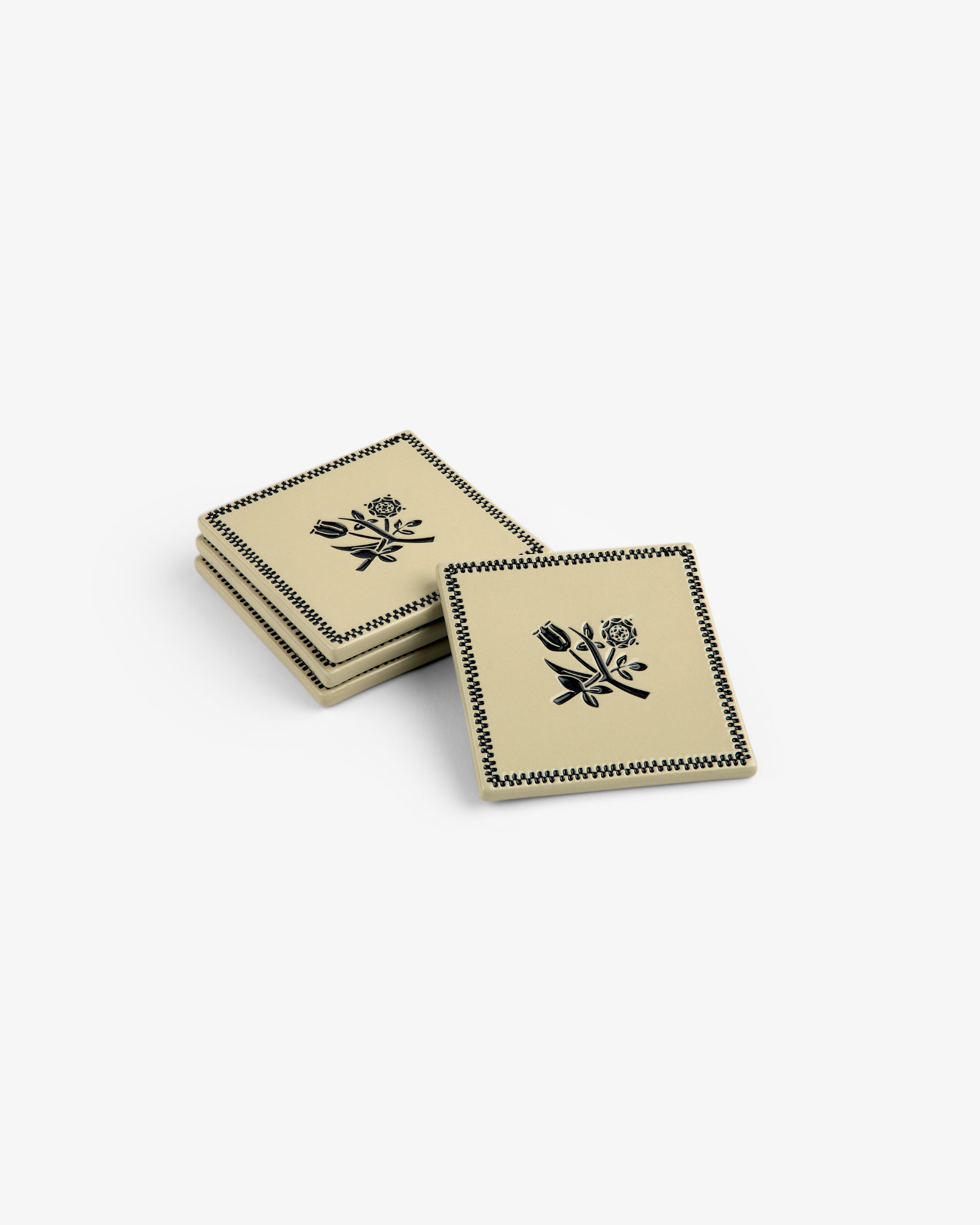 Set of 4 Crest Coasters: beige squares with black floral designs and patterned borders, stacked on a white background.