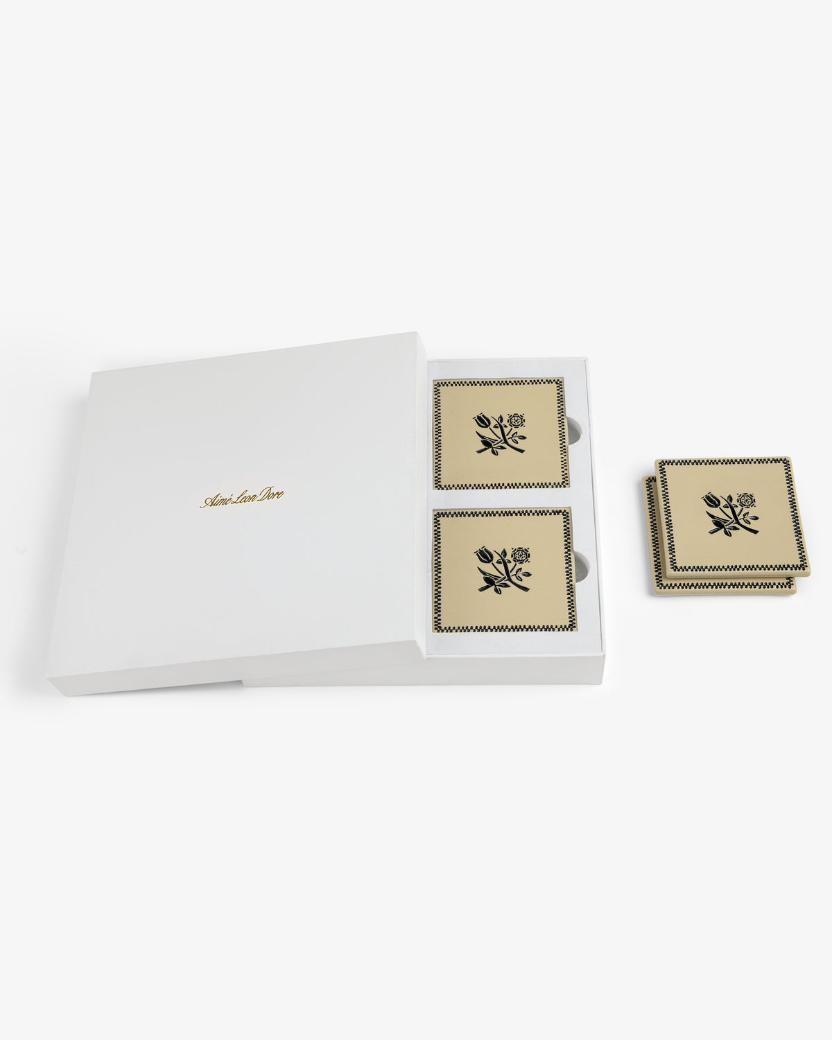 The Crest Coaster (Set of 4) comes in a white box with gold text, featuring square beige coasters with black florals.